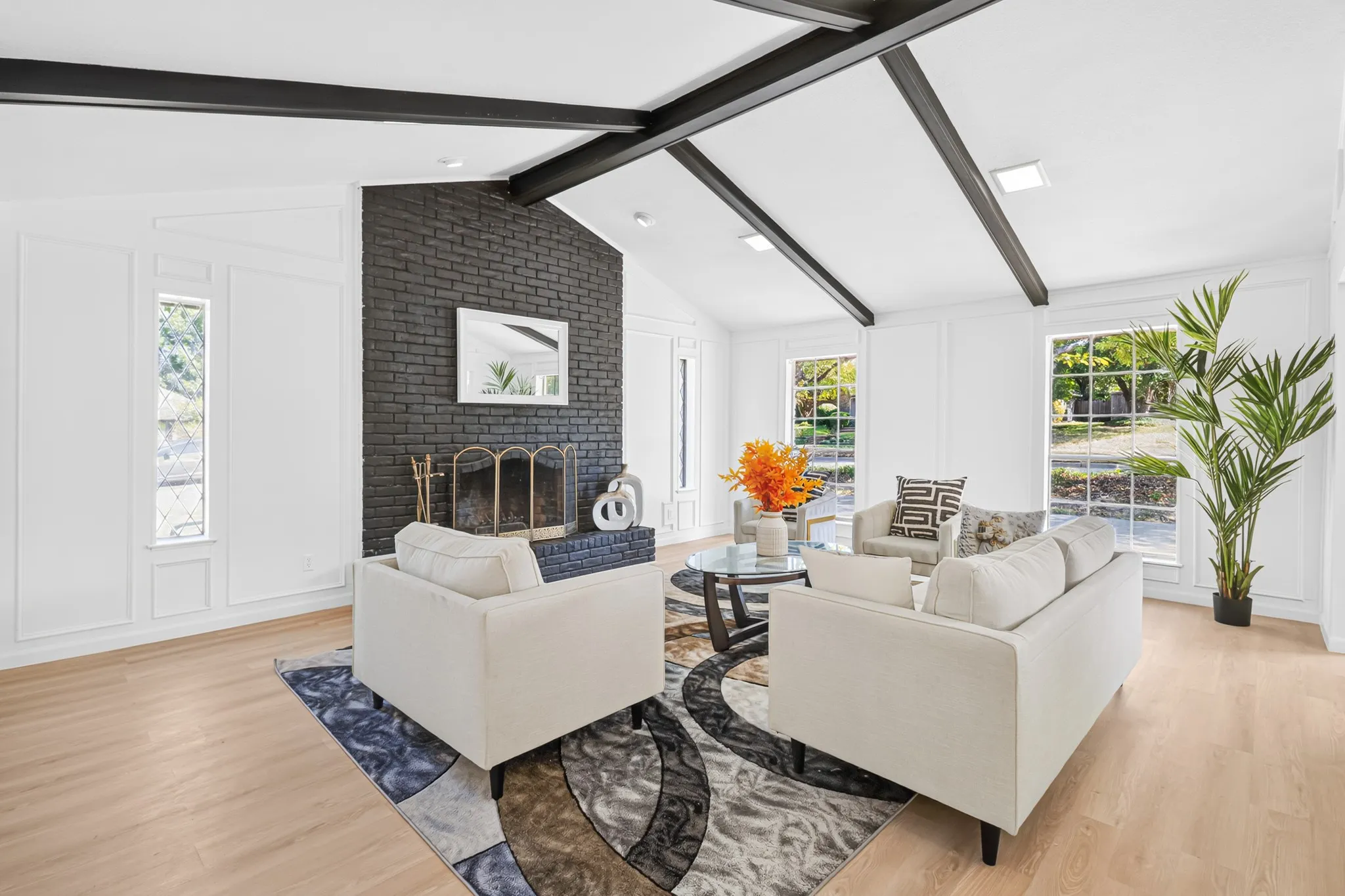 Vaulted ceiling with exposed beams, wood-finish flooring, black brick fireplace with a hearth, window paneling, and multiple windows
