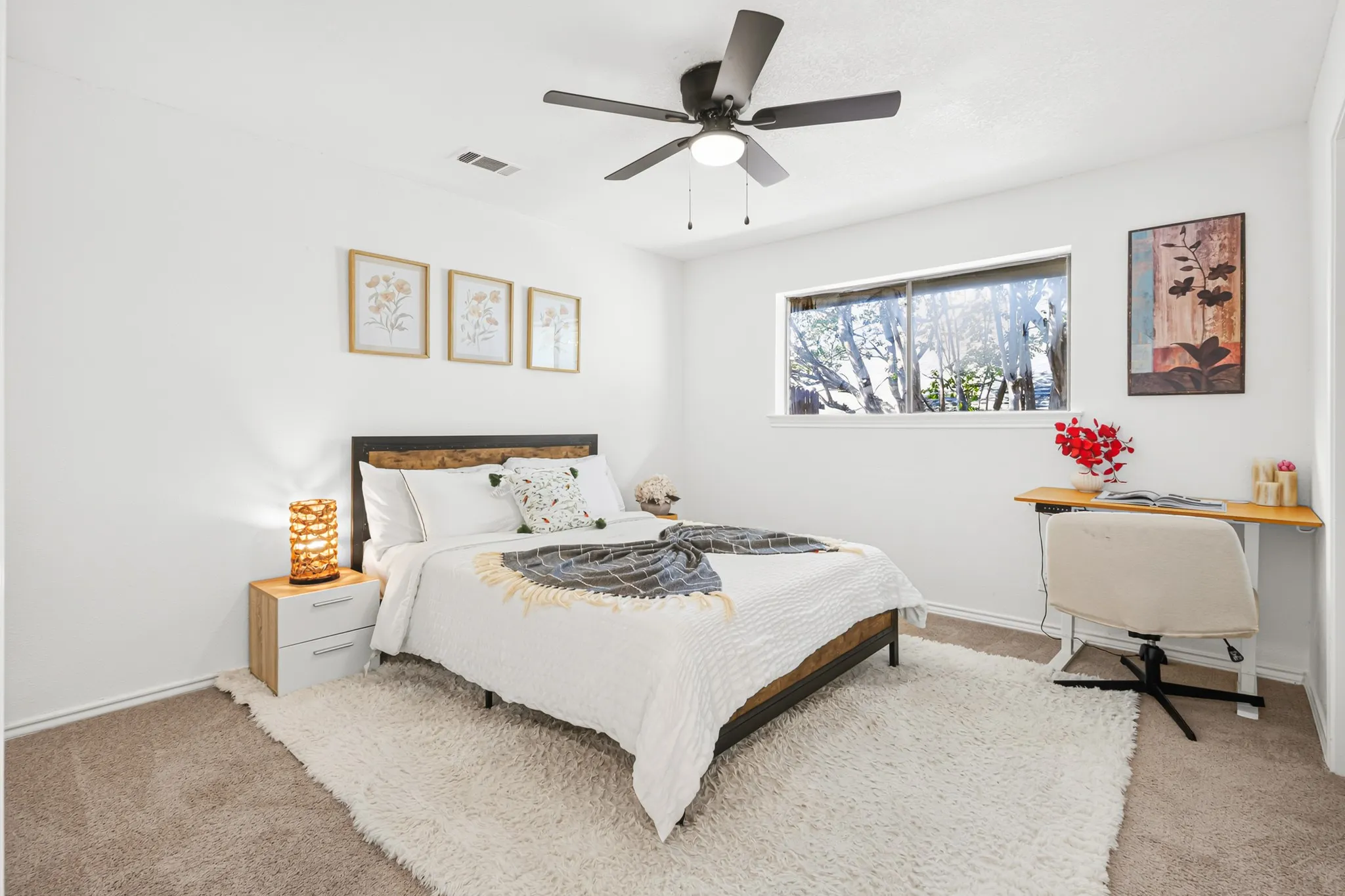 Bright secondary bedroom featuring a wood-finish bed frame, neutral carpet flooring, and large windows with natural light