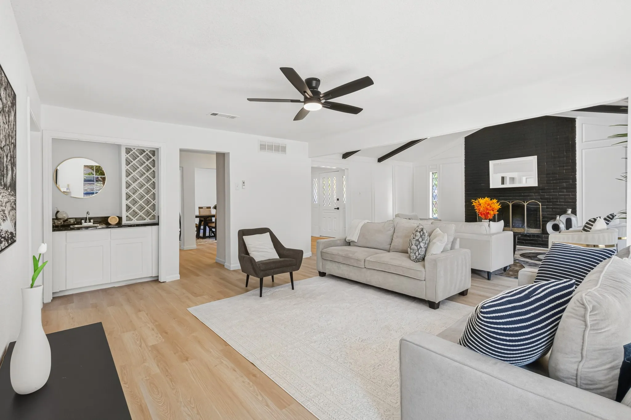 Wood-finish flooring, built-in wet bar with cabinetry, vaulted ceiling with exposed beams, brick fireplace with black finish, and a ceiling fan