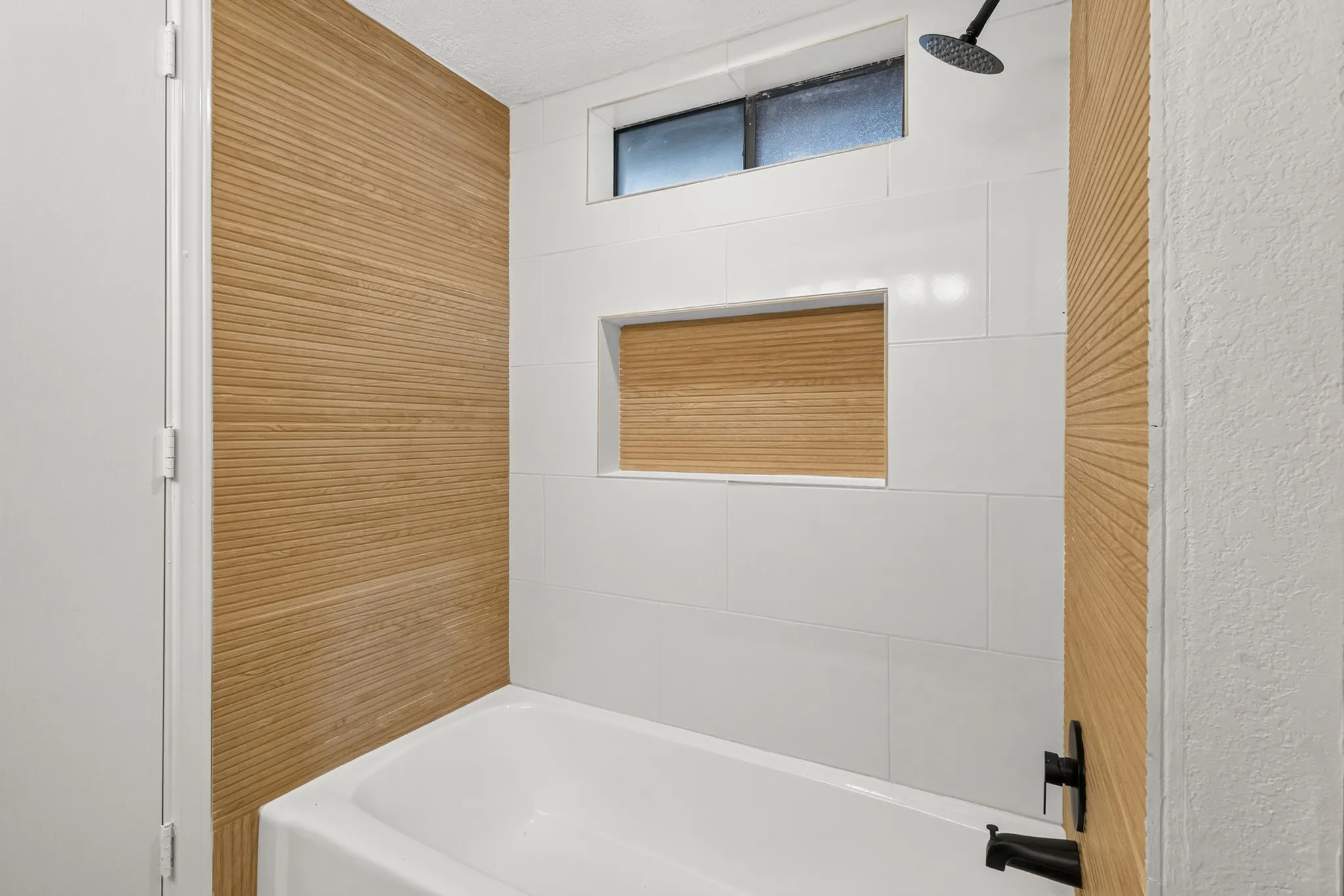 Bathtub with white tile surround, integrated shower niche, and matte black fixtures