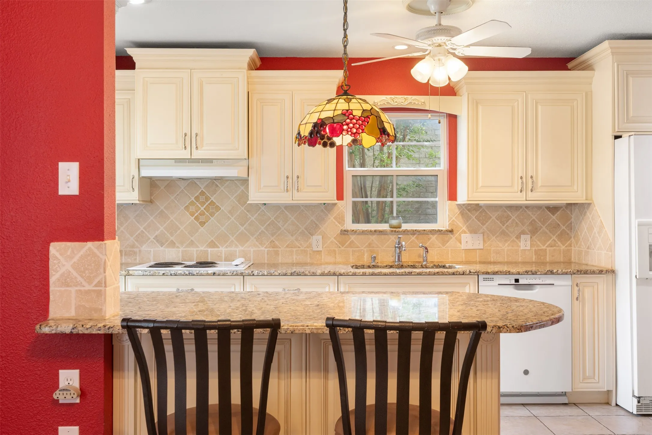 A diagonally laid (diamond-pattern) tumbled travertine backsplash with coordinating accent insets. The tumbled finish gives it a warm, timeless, Old World character that complements a wide range of design styles. The Granite is a 3CM Santa Cecilia Granite, with raised panel cream cabinetry and crown moulding exude elegance found in custom homes.