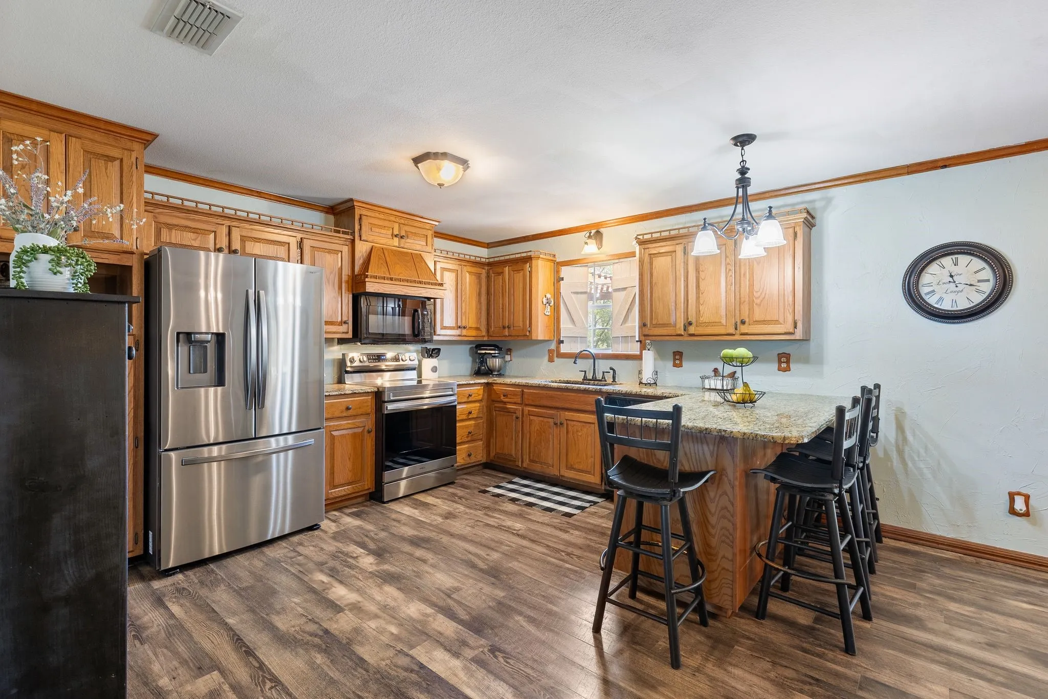 Kitchen with a breakfast bar, kitchen peninsula, appliances with stainless steel finishes, crown molding, and dark wood-type flooring