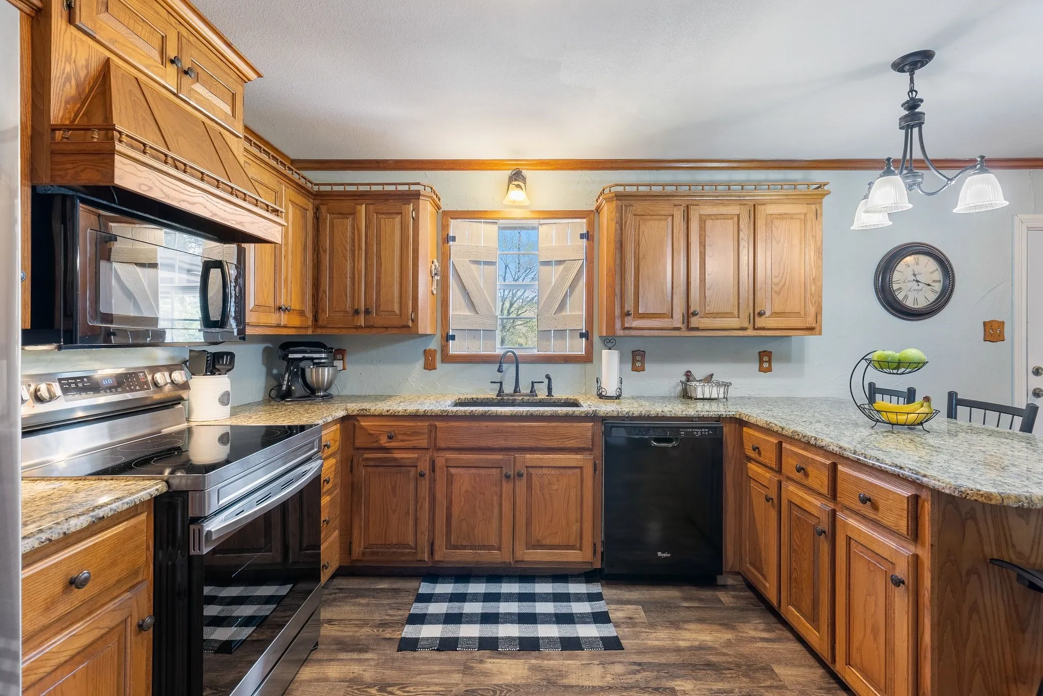 Kitchen with stainless steel electric range, black dishwasher, sink, dark wood-type flooring, and kitchen peninsula