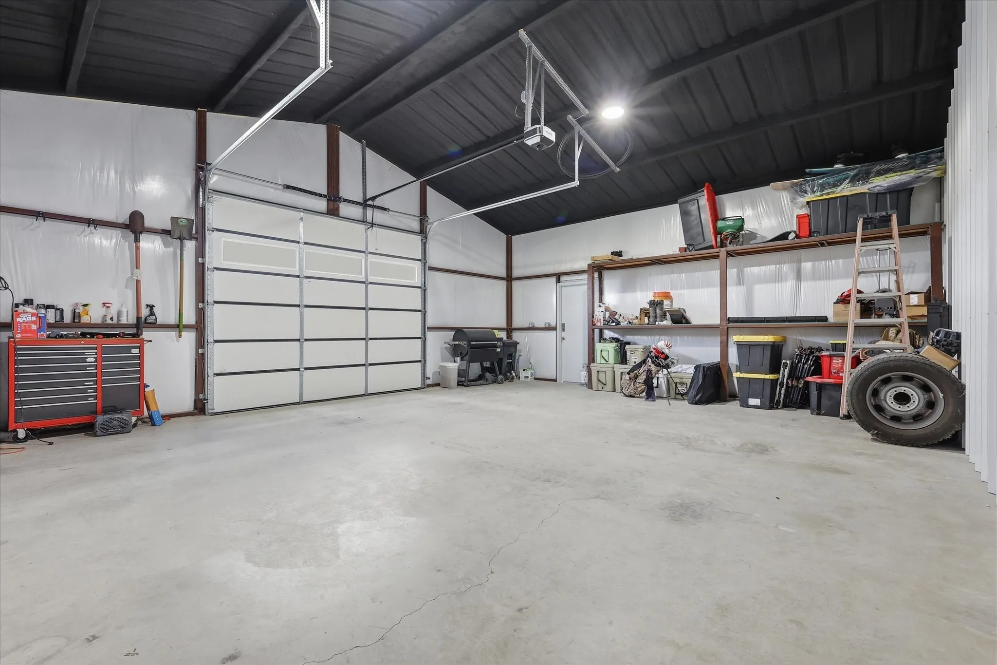 Spacious metal building featuring a large overhead door, concrete flooring, exposed metal framing, and a high ceiling