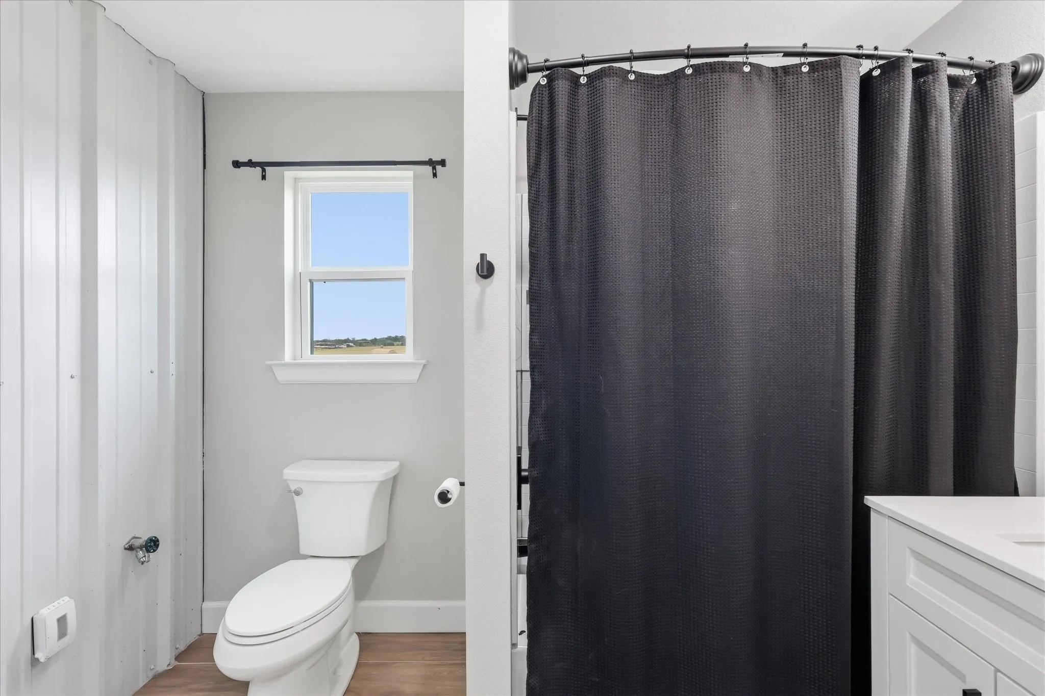 Bathroom featuring light wood-finish flooring, a white toilet, and a window with a black curtain rod