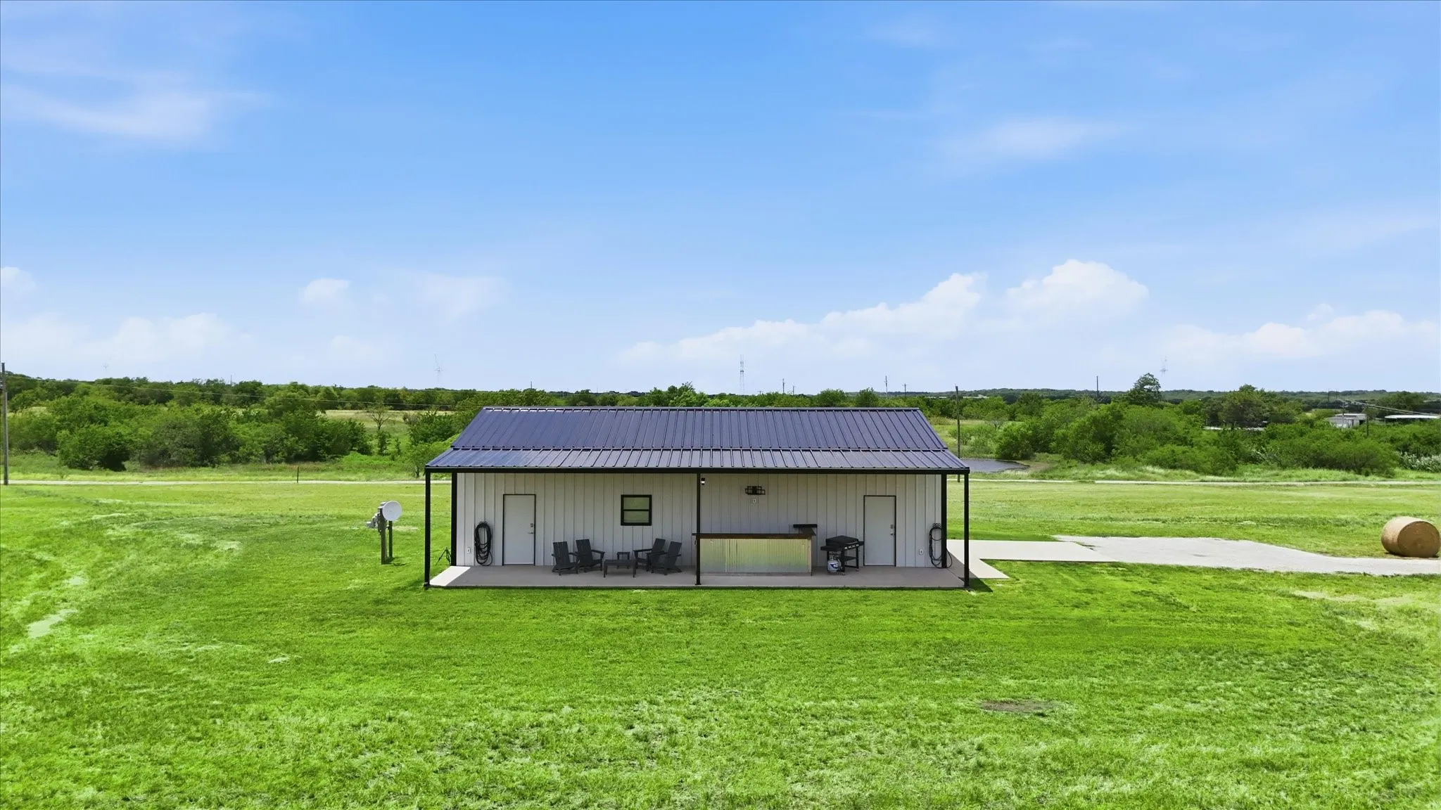 Metal-roofed structure featuring a covered outdoor living area with concrete flooring, an attached outdoor kitchen, and a concrete driveway