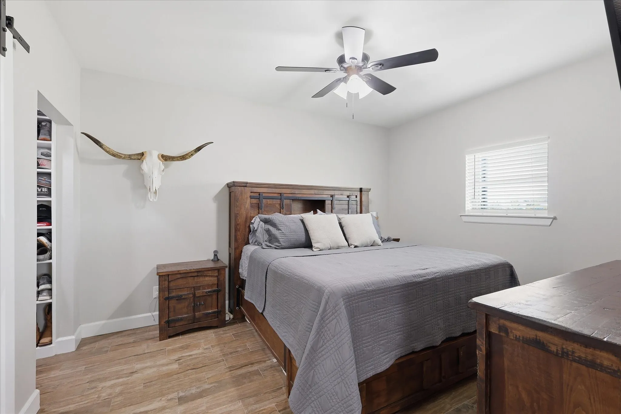 Spacious room featuring wood-finish flooring, a ceiling fan with integrated lighting, and a window with blinds
