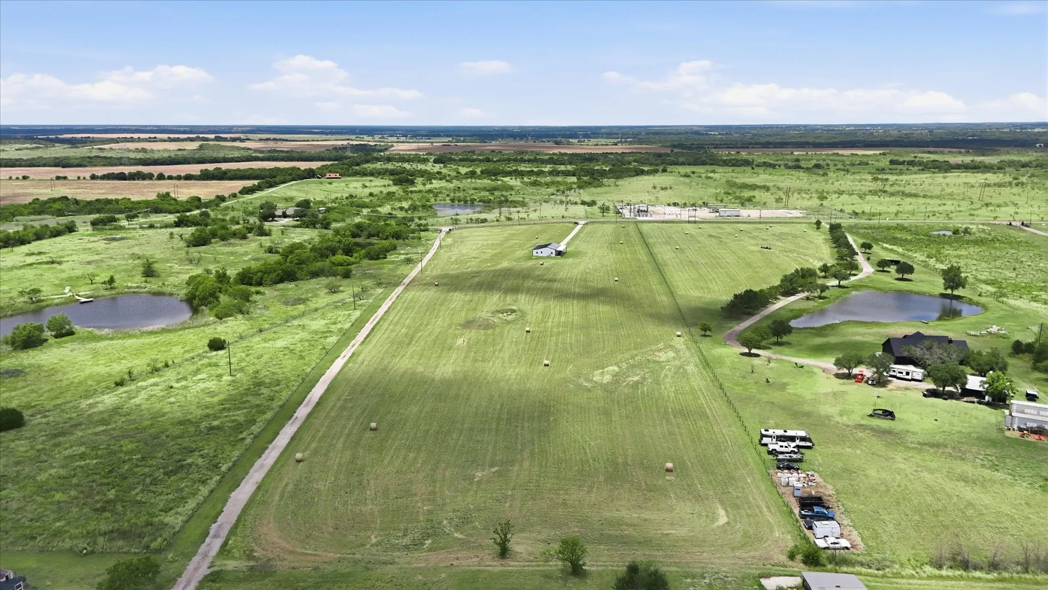 Expansive rural land featuring clear skies, distant tree lines, multiple ponds, and a mix of cultivated fields and green spaces