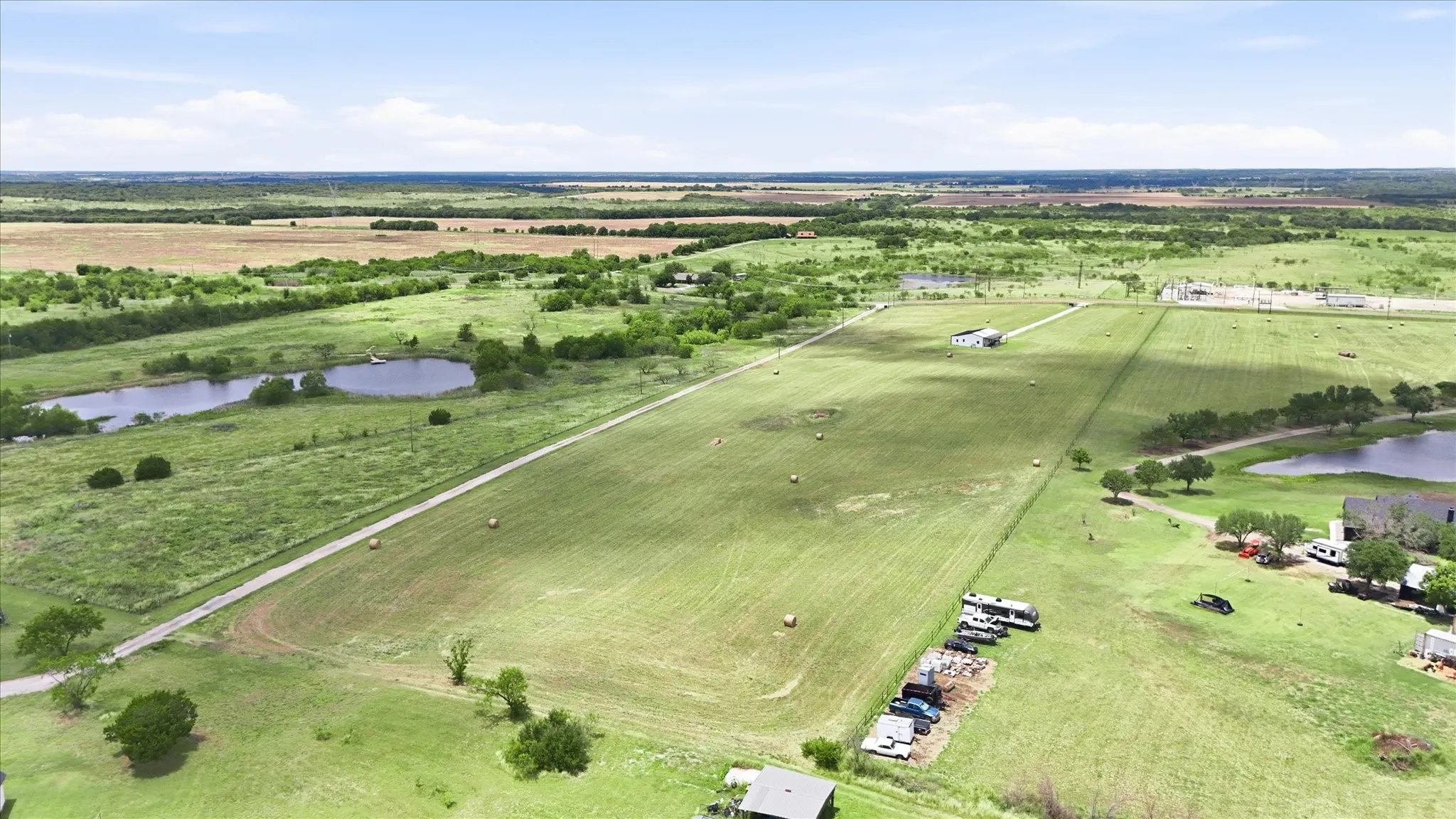 Expansive rural property featuring a large open field, two distinct ponds, an unpaved access road, and scattered mature trees