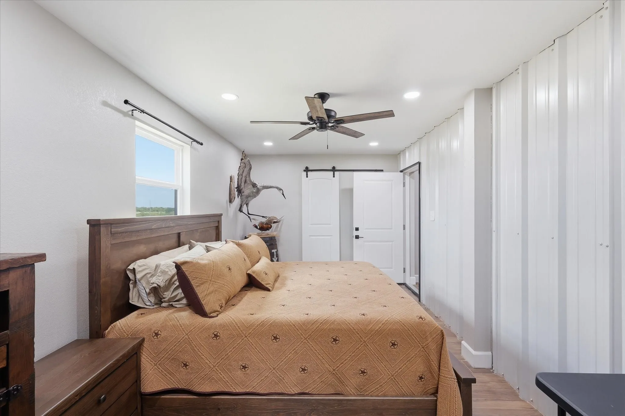 Spacious bedroom featuring wood-finish flooring, a contemporary ceiling fan, recessed lighting, and a window providing natural light