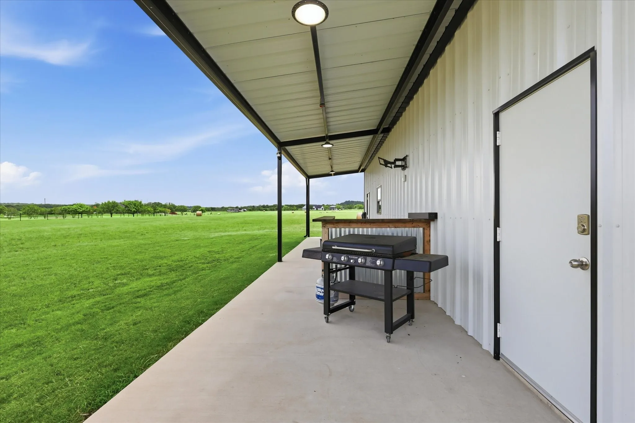 Covered outdoor patio with concrete flooring, accented by a corrugated metal wall and a built-in outdoor bar