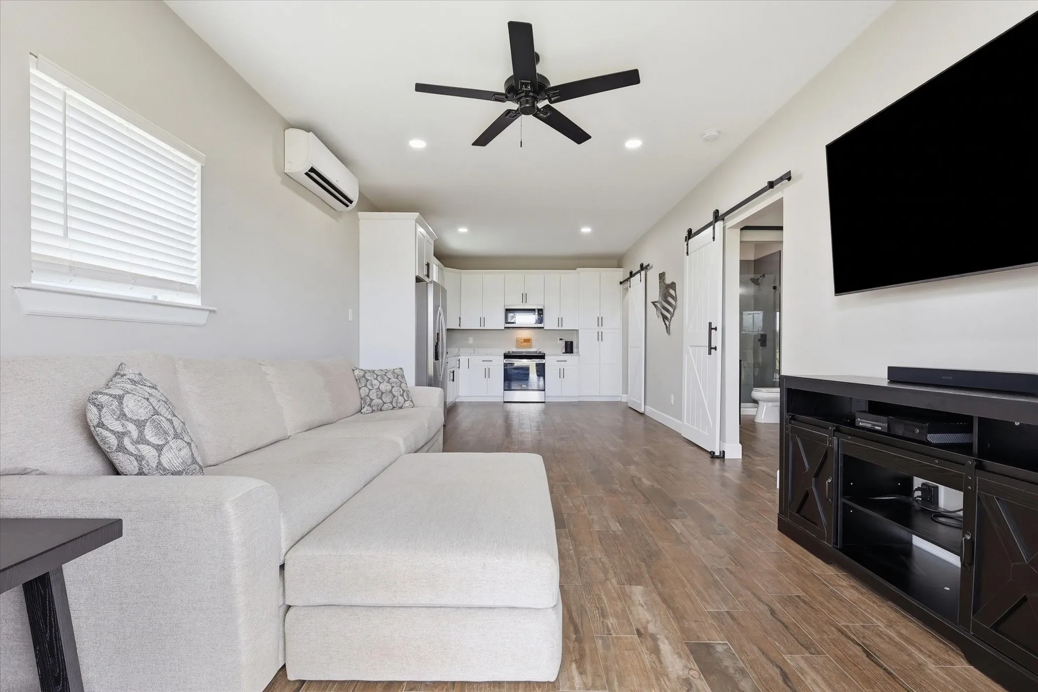 Open-concept living area featuring wood-finish flooring, a contemporary ceiling fan, recessed lighting, white kitchen cabinetry, and barn doors