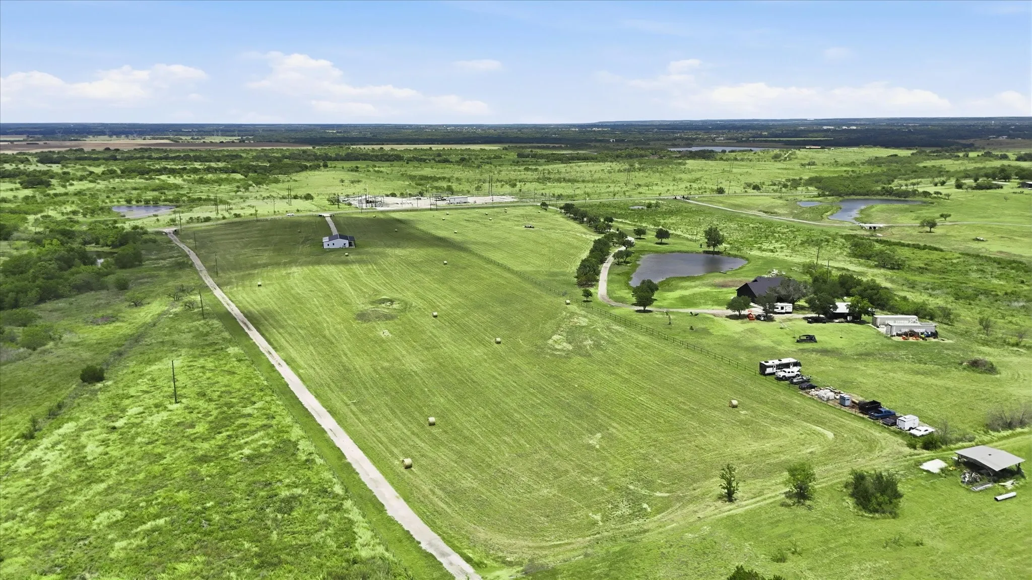 Expansive rural property featuring a long driveway, multiple structures, and a private pond