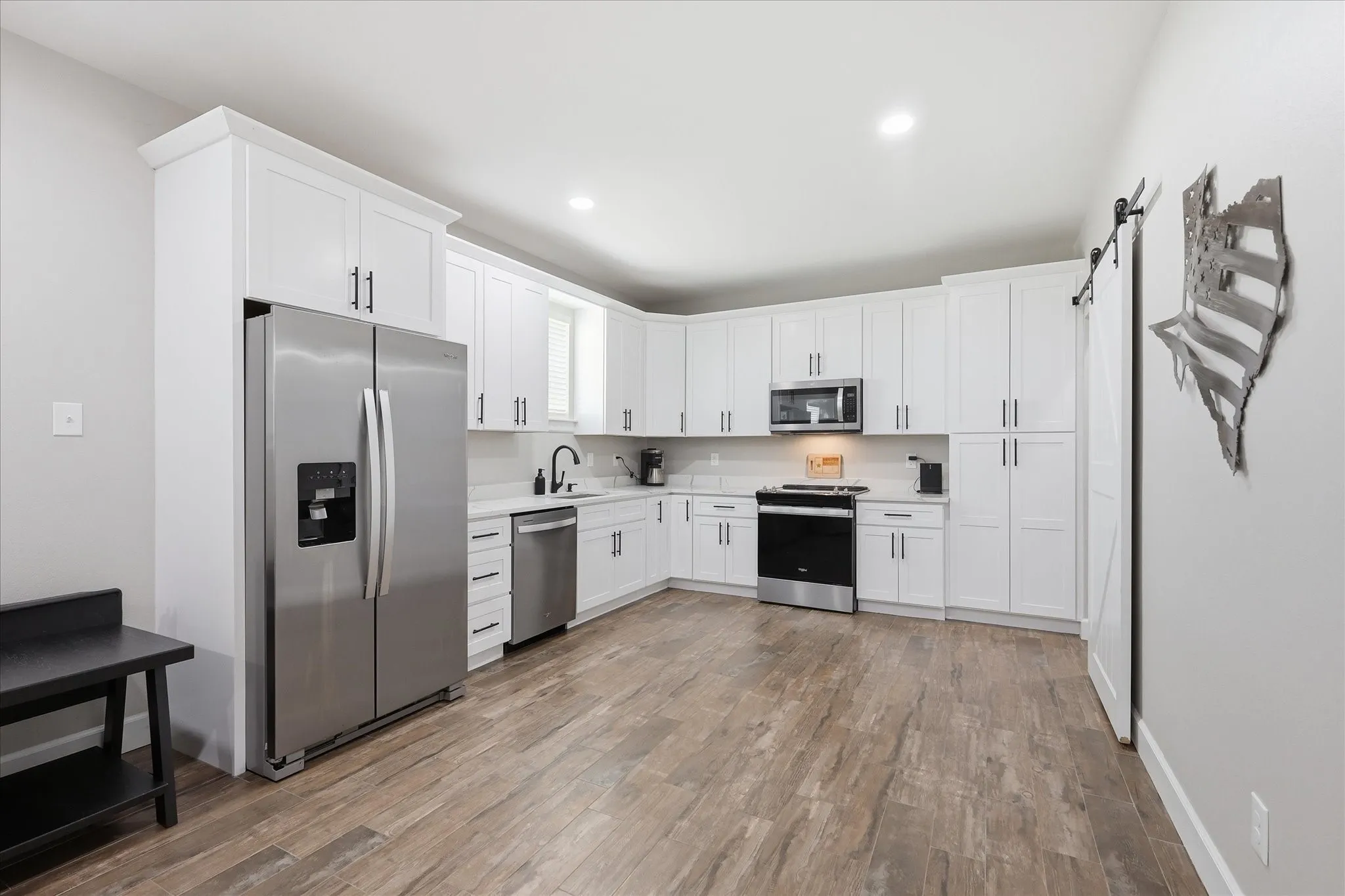 Modern kitchen featuring white shaker cabinetry, stainless steel appliances, light countertops, wood-finish flooring, and recessed lighting