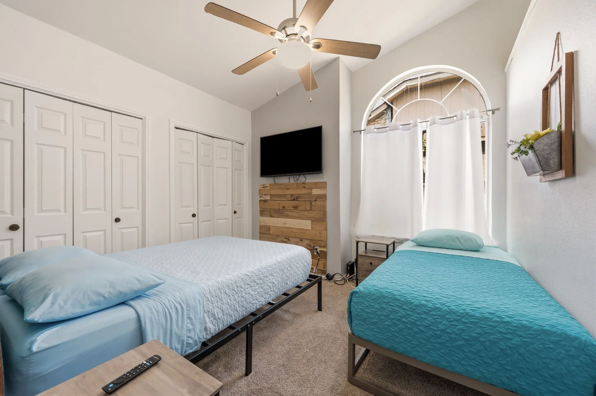 Arched window with upper transom, vaulted ceiling, wood-finish accent wall, and ceiling fan with light fixture