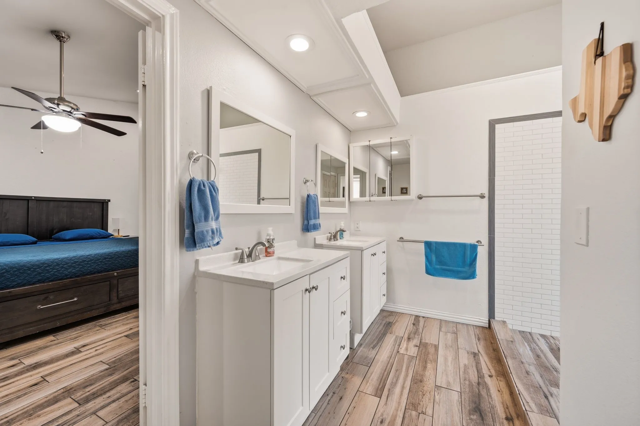 Dual vanity with white cabinetry and integrated sinks, wood-finish flooring, recessed lighting, and a subway tile shower enclosure