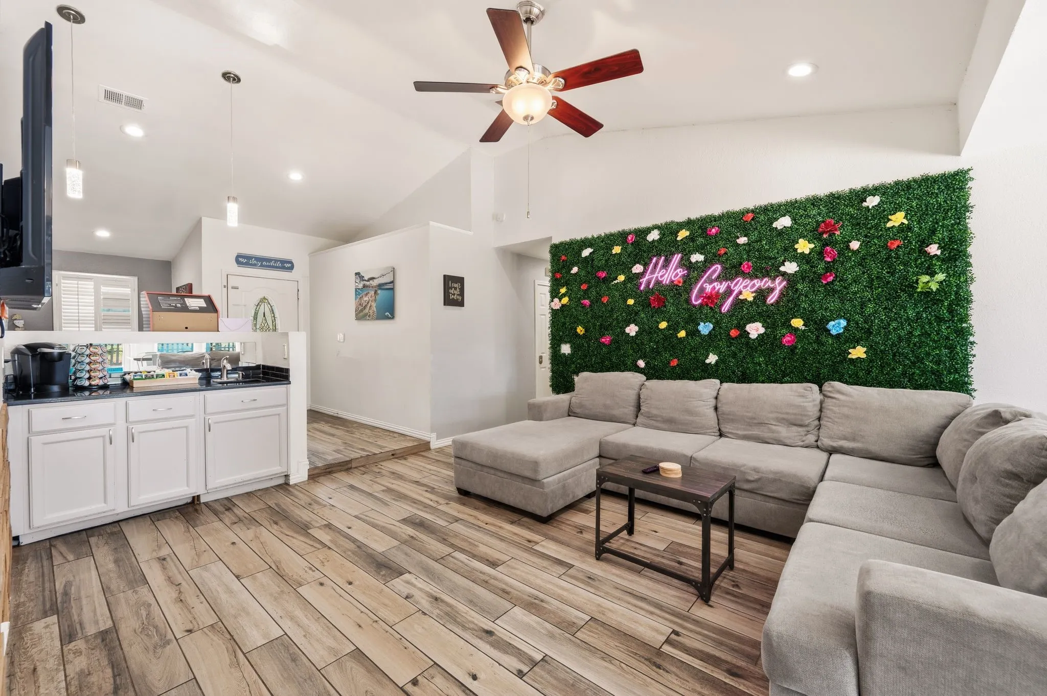 Open-concept living space featuring vaulted ceilings, wood-finish flooring, and a built-in coffee bar with white cabinetry and a dark countertop