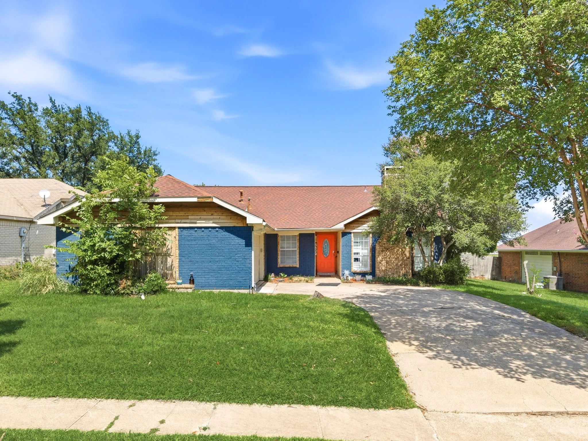Single-story residence featuring a striking orange entry door, blue exterior siding, and natural stone accents