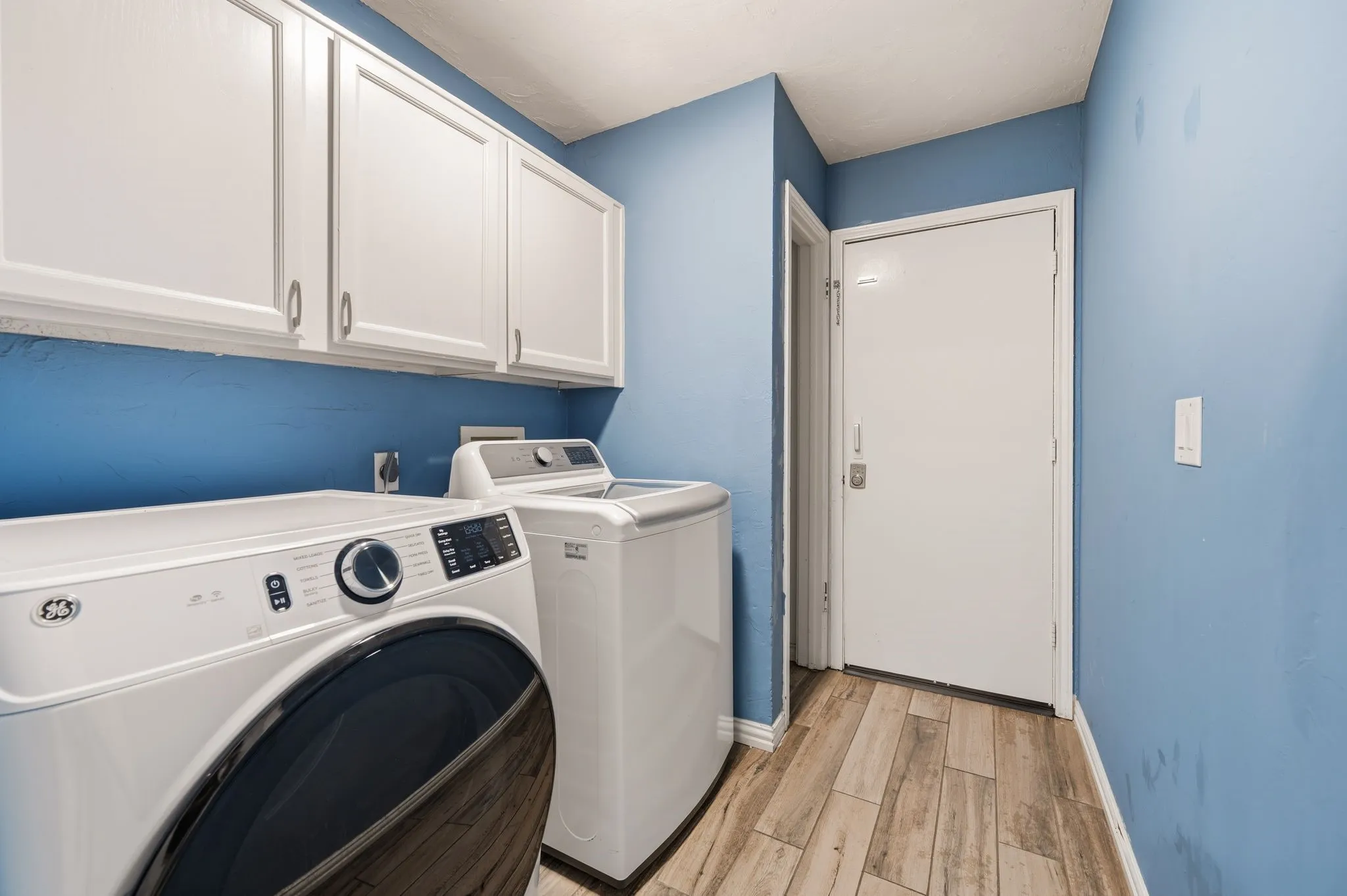 Laundry area featuring overhead white cabinetry and wood-finish tile flooring