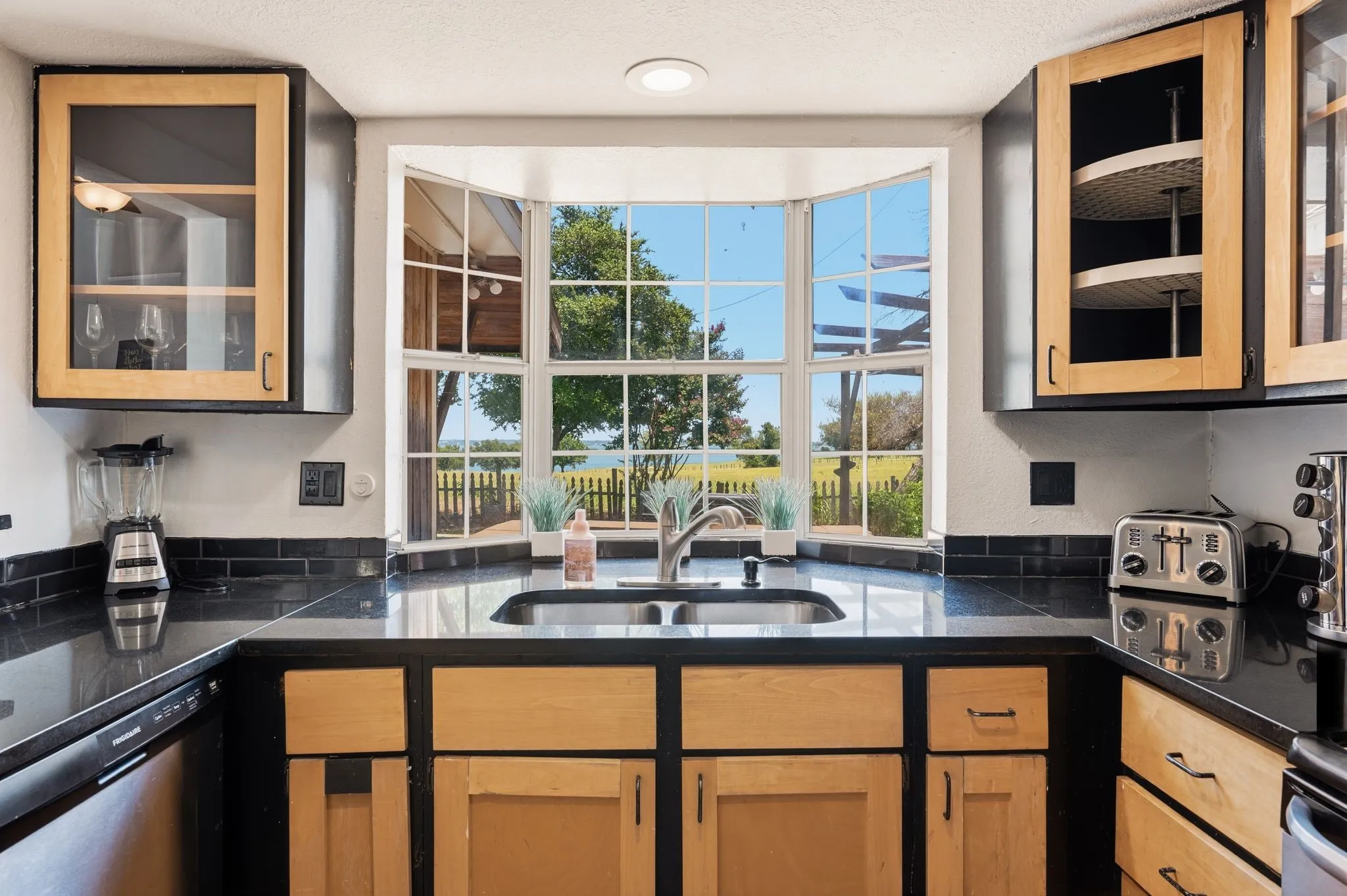 Kitchen featuring a bay window, wood-finish cabinetry, dark countertops, a dark tile backsplash, and an undermount sink
