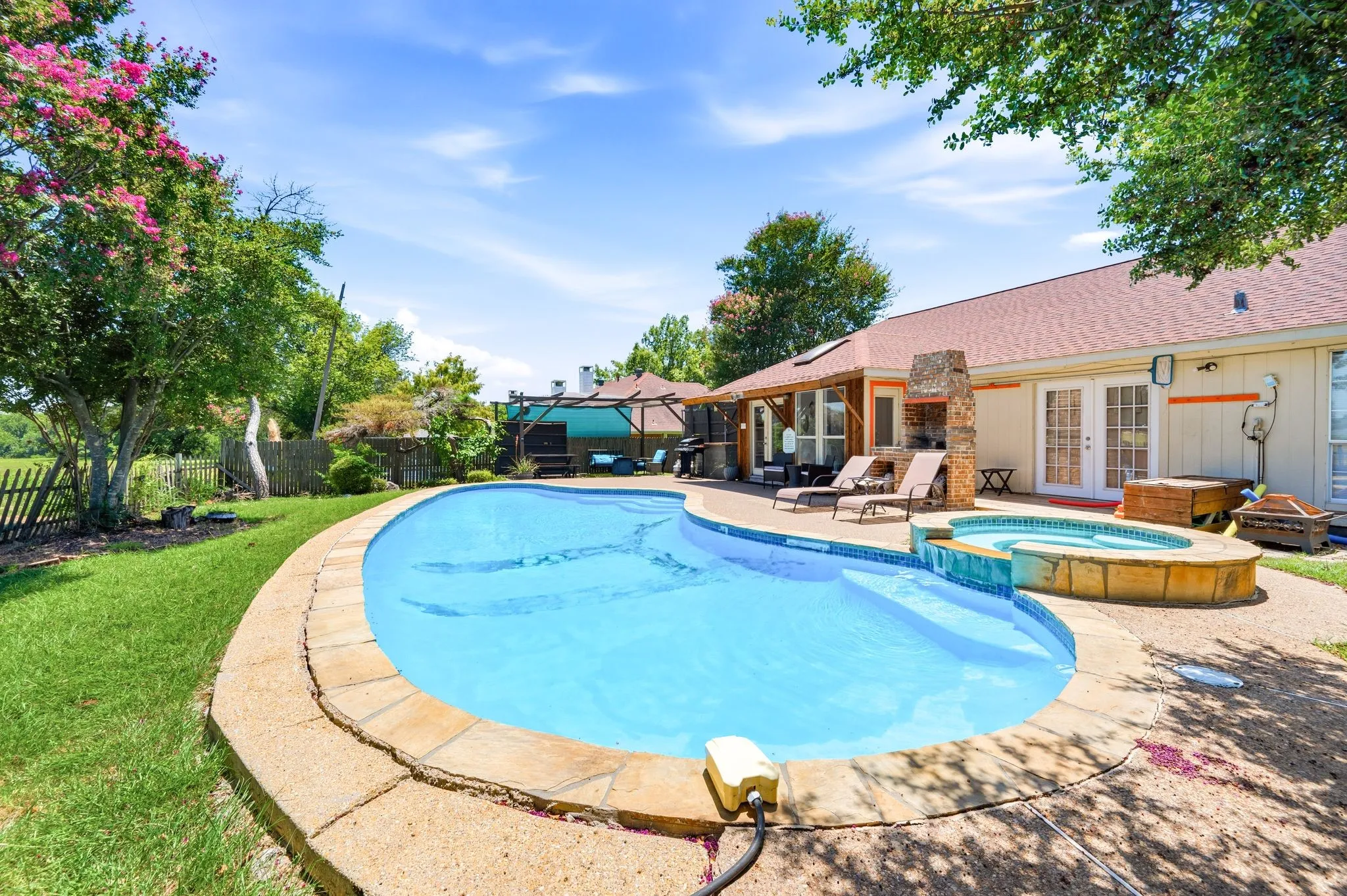 Expansive backyard featuring a freeform swimming pool with integrated spa, concrete decking, and a stone-clad outdoor​​‌​​​​‌​​‌‌​‌‌​​​‌‌​‌​‌​‌​​​‌​​ fireplace
