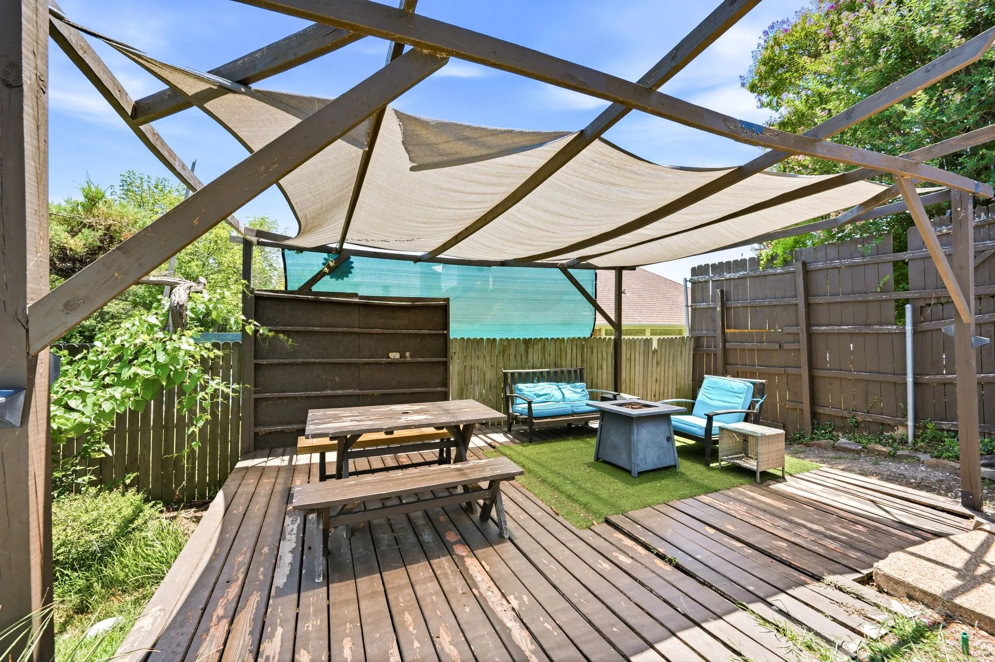 Expansive backyard deck featuring a wood pergola with shade sails, a designated artificial turf area, and privacy fencing