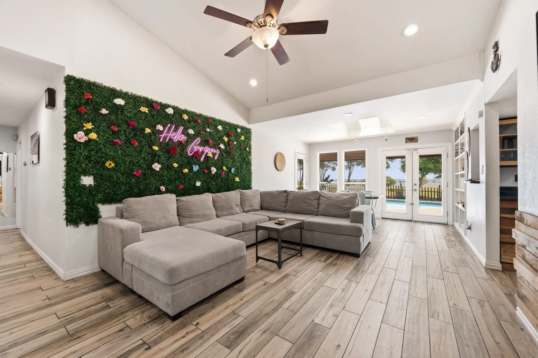 Spacious living area featuring vaulted ceilings, wood-finish flooring, recessed lighting, and a decorative green wall accent