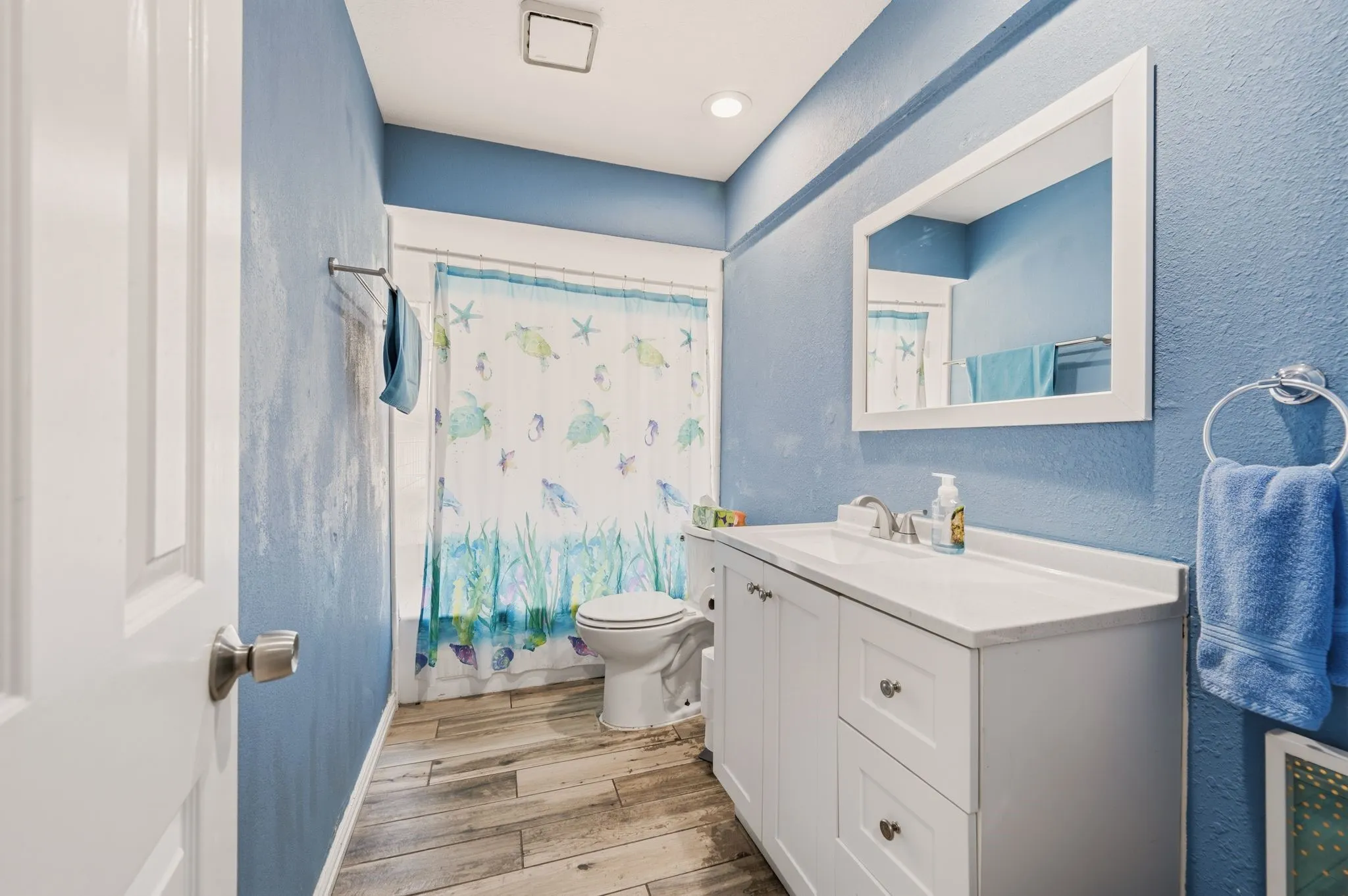 Bathroom featuring wood-finish flooring, a white vanity with integrated sink, a rectangular framed mirror, and a toilet with a shower/tub combination