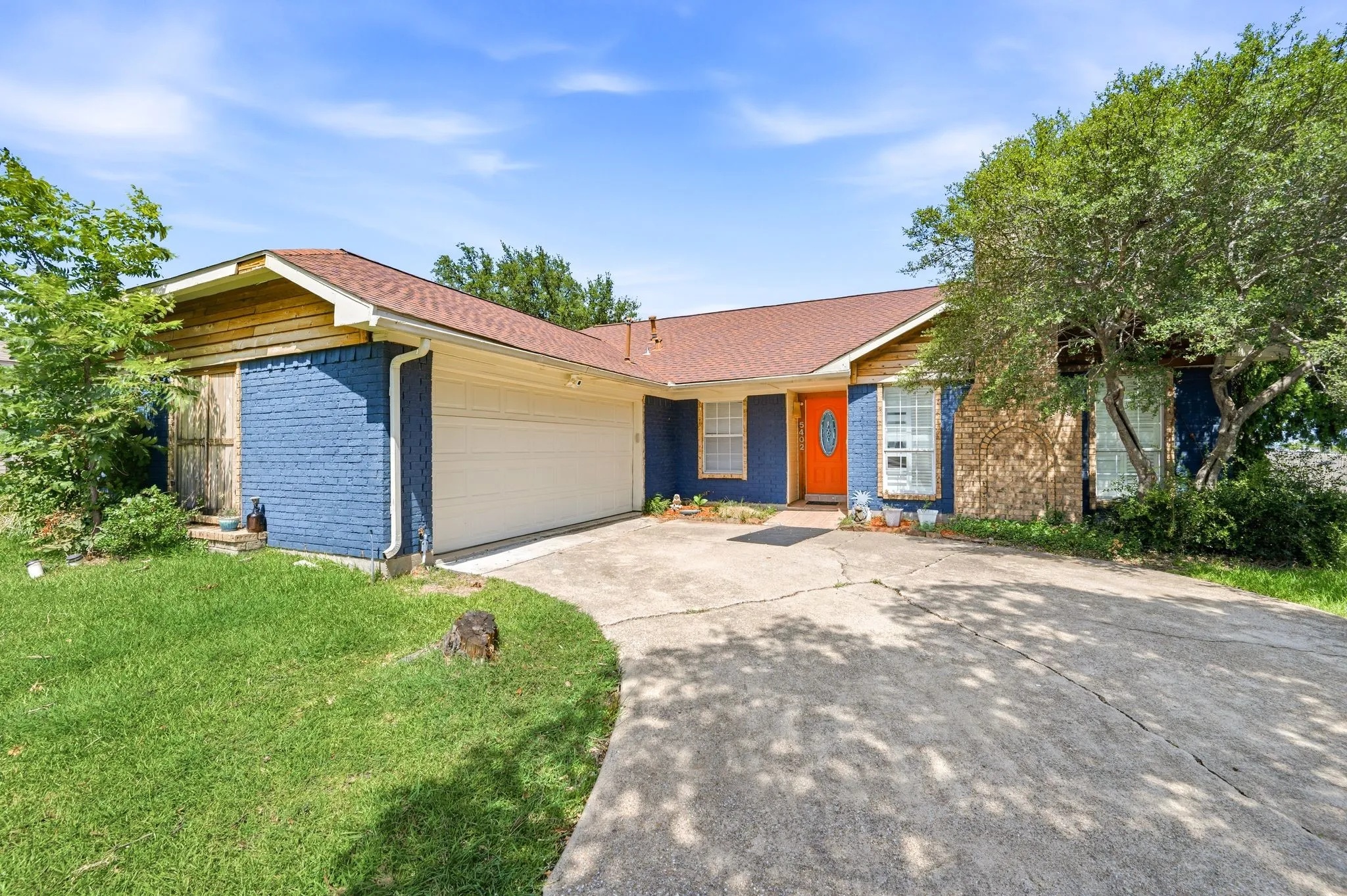 Single-story residence featuring a two-car garage, brick and wood siding, and a vibrant orange front door