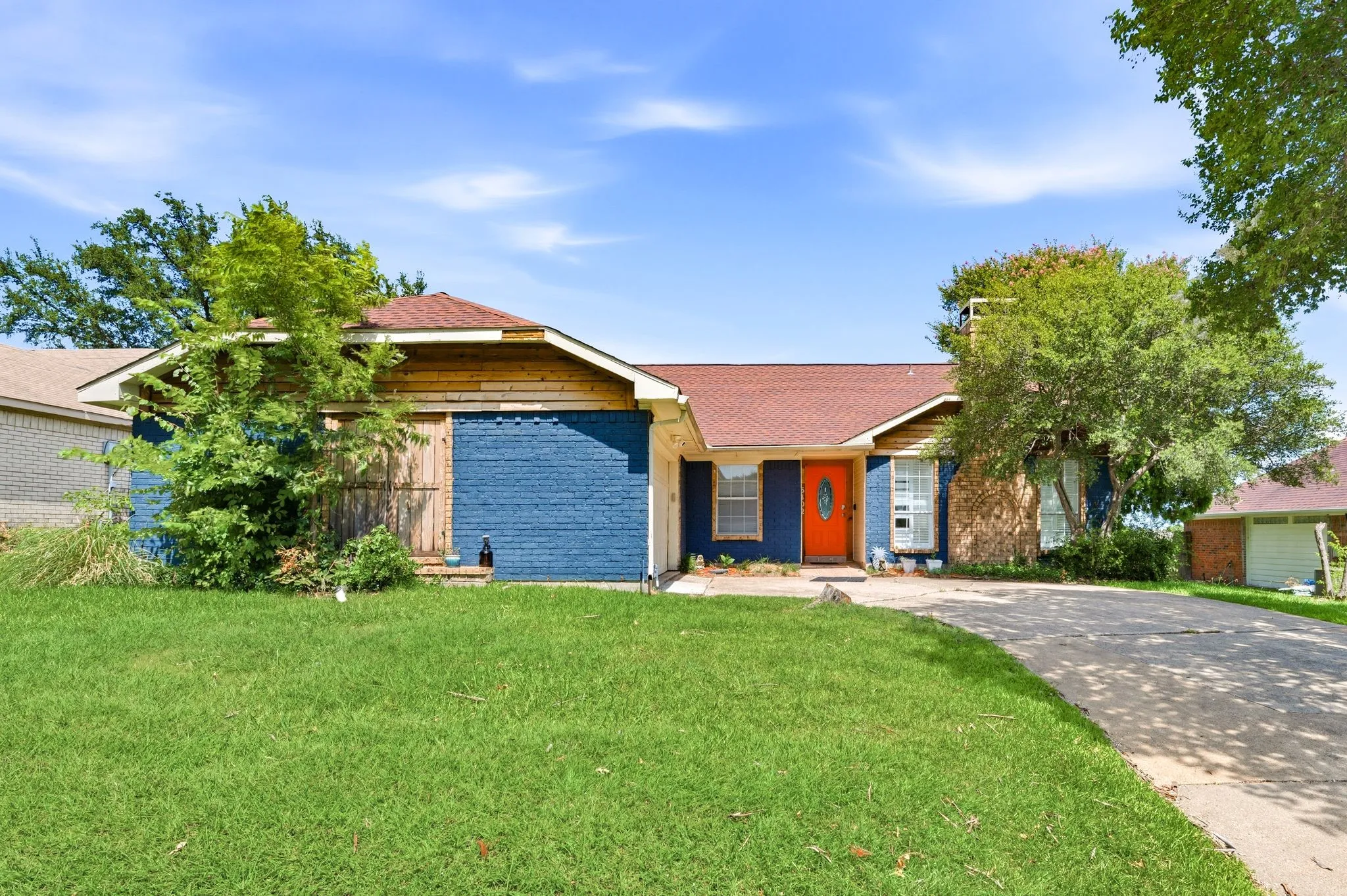 Ranch-style exterior with a red roof, vibrant orange front door, blue-painted brick, and natural wood siding accents