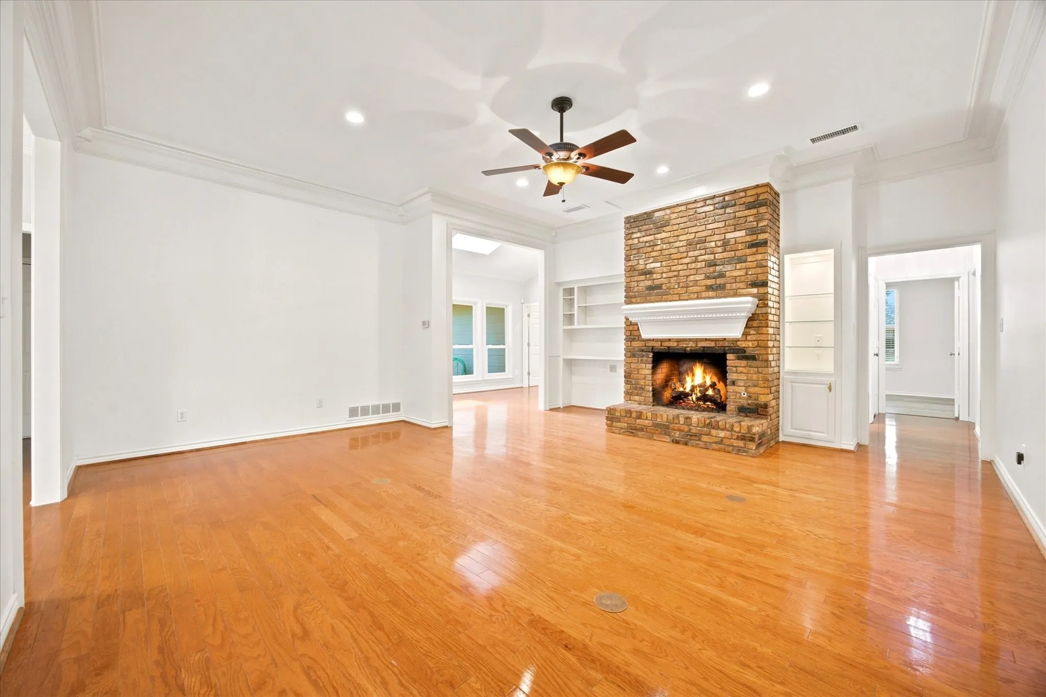Spacious room featuring wood-finish flooring, a brick fireplace with a white mantel, built-in shelving, a ceiling fan, and recessed lighting