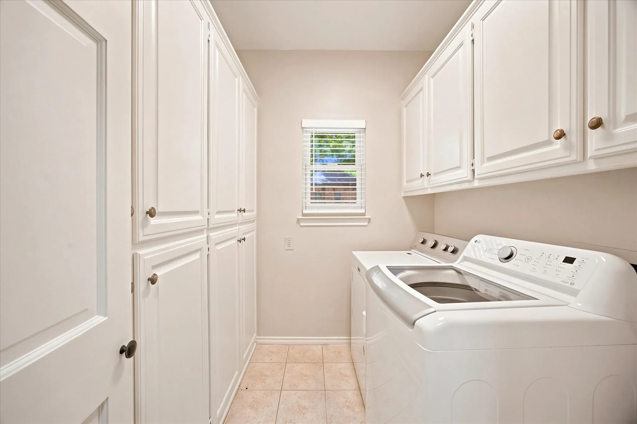 Dedicated utility space featuring extensive white cabinetry, a built-in countertop, and a window with blinds
