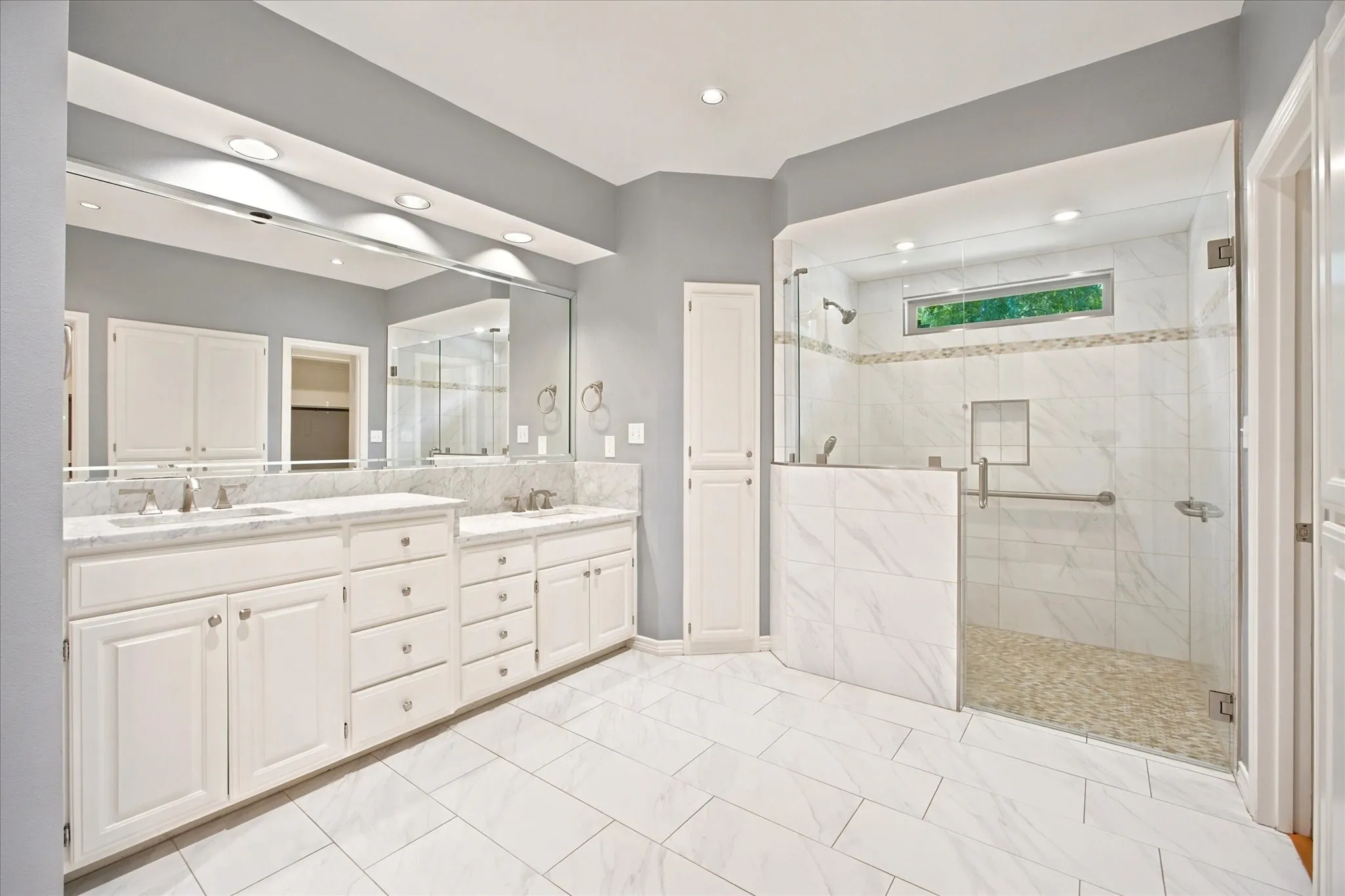 Spacious bathroom featuring a dual vanity with white cabinetry and stone countertops, an oversized mirror, and recessed lighting
