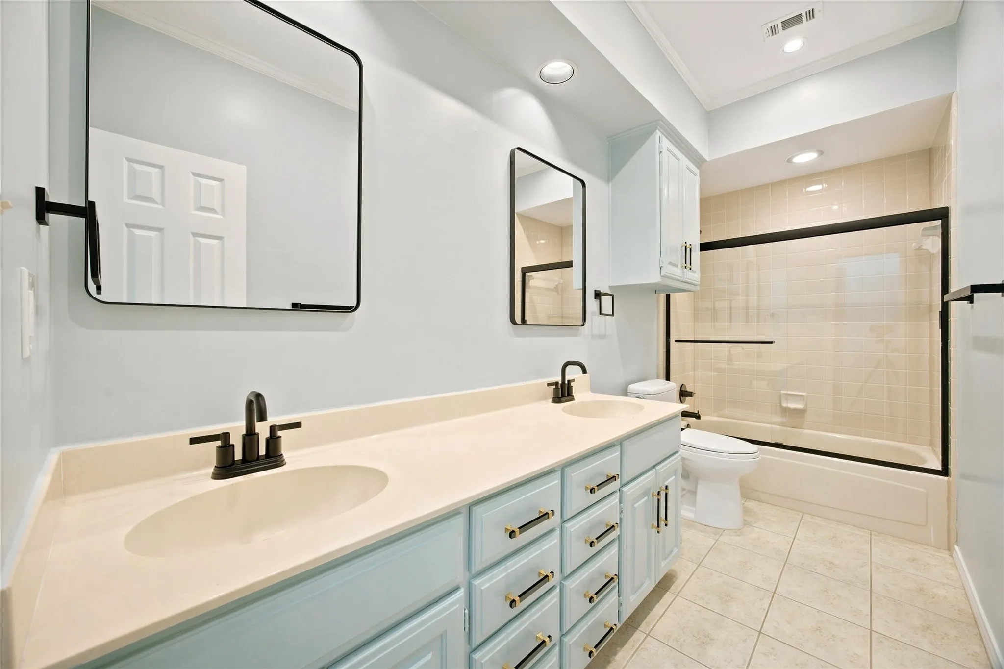 Bathroom featuring a light blue dual vanity with gold-tone hardware, matte black faucets, and a light-colored countertop