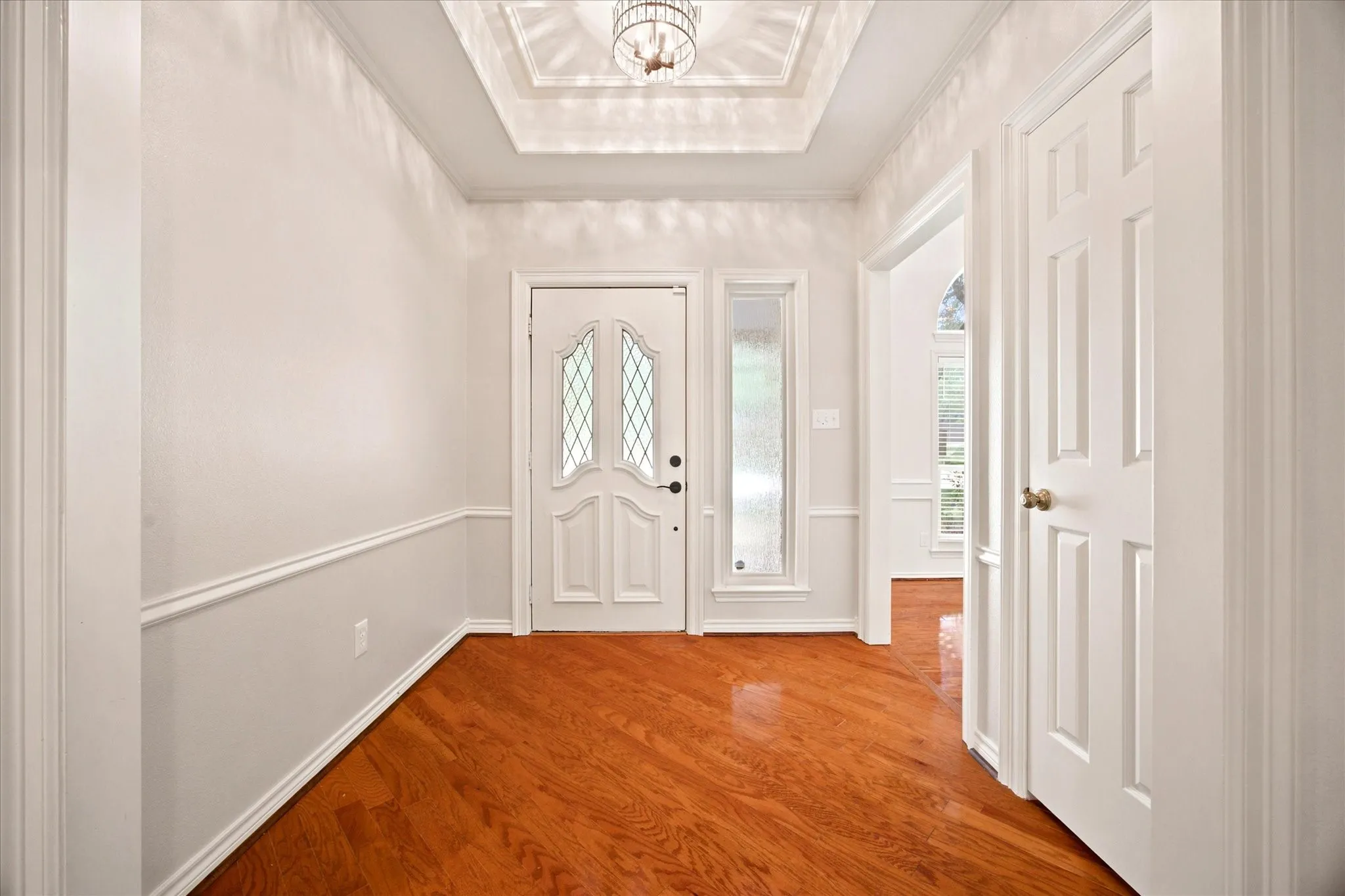 Inviting entry hall featuring wood-finish flooring, wainscoting, and a decorative coffered ceiling with a chandelier