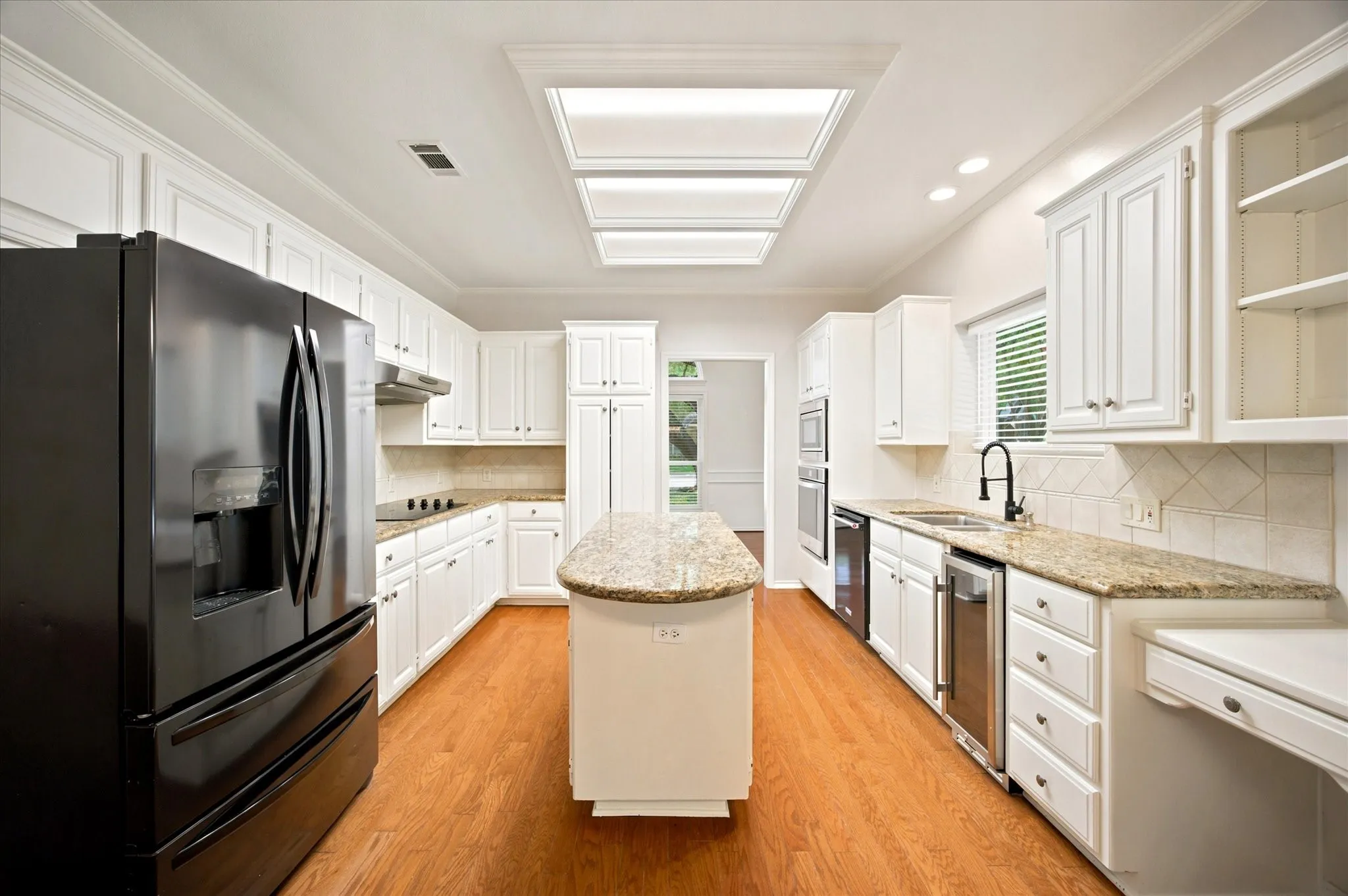 Bright kitchen featuring white cabinetry, granite countertops, wood-finish flooring, a central island, and a skylight