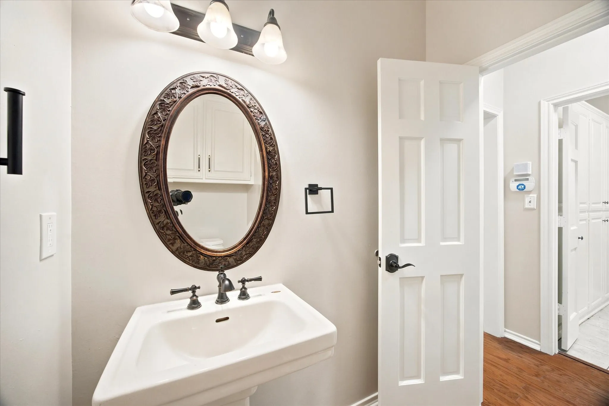 Pedestal sink with dark bronze faucet and an ornate oval mirror