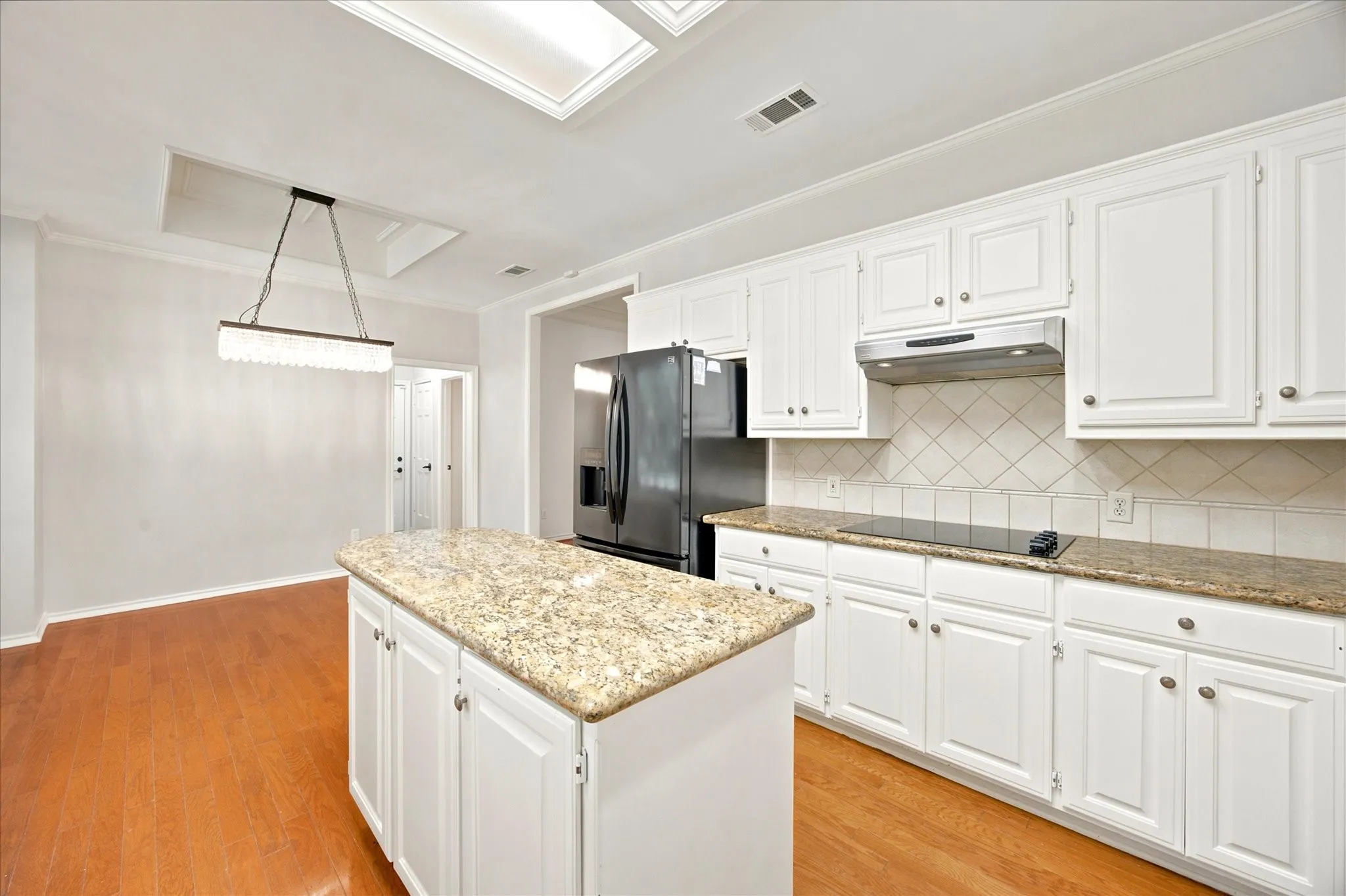 Kitchen featuring white cabinetry, granite countertops, tile backsplash, built-in electric cooktop, and an island with additional storage