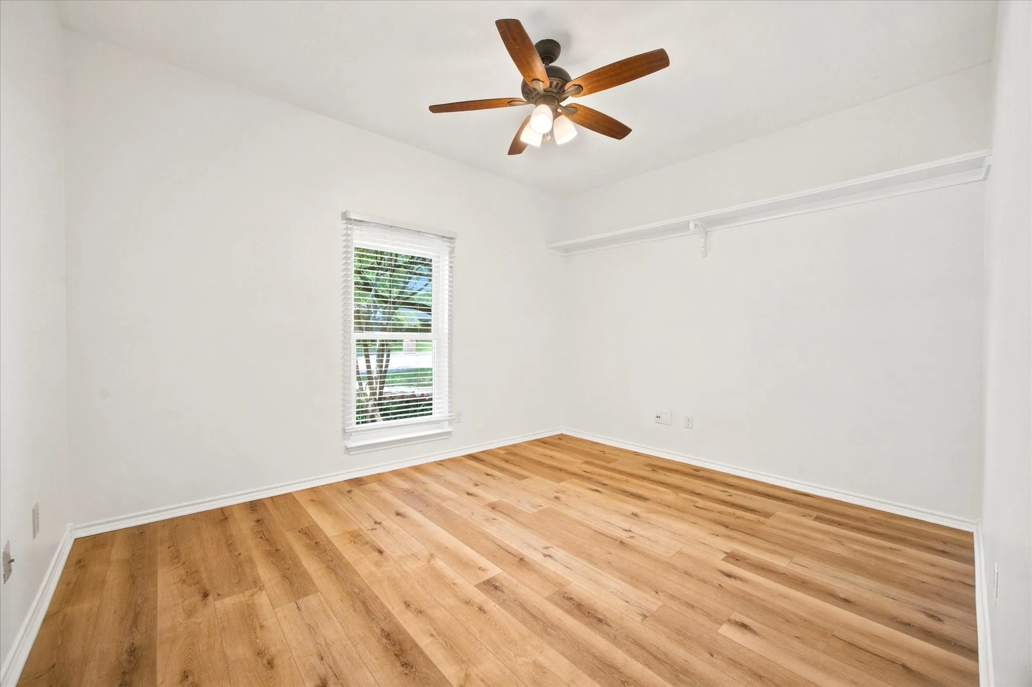 Bright room featuring wood-finish flooring, a window with blinds, and a ceiling fan with integrated lighting
