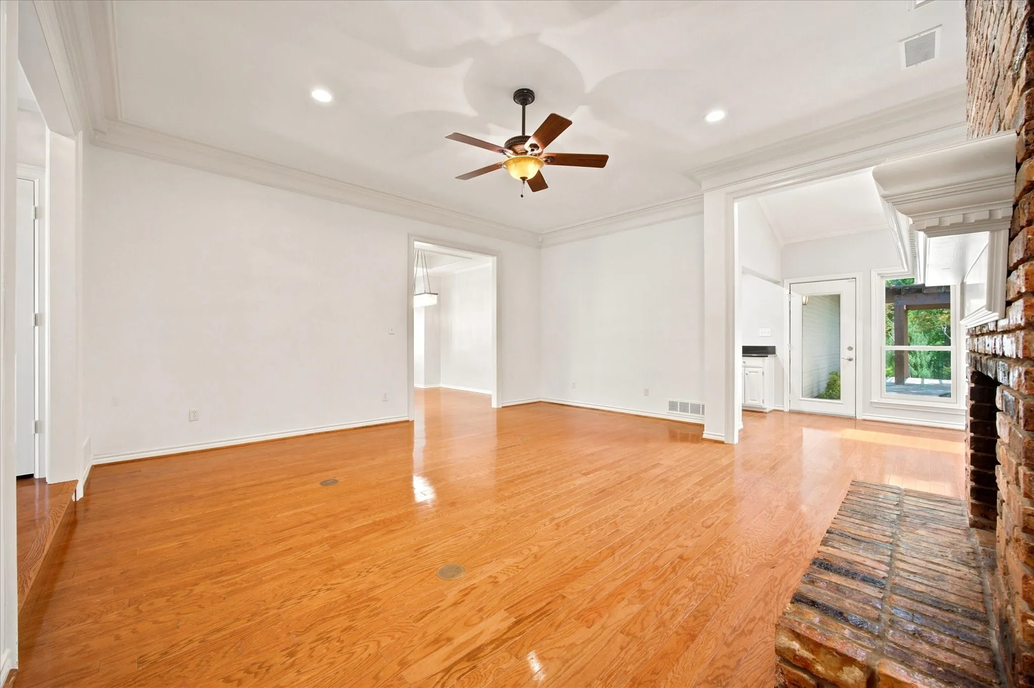 Spacious room featuring wood-finish flooring, a brick fireplace with a white mantel, and crown molding