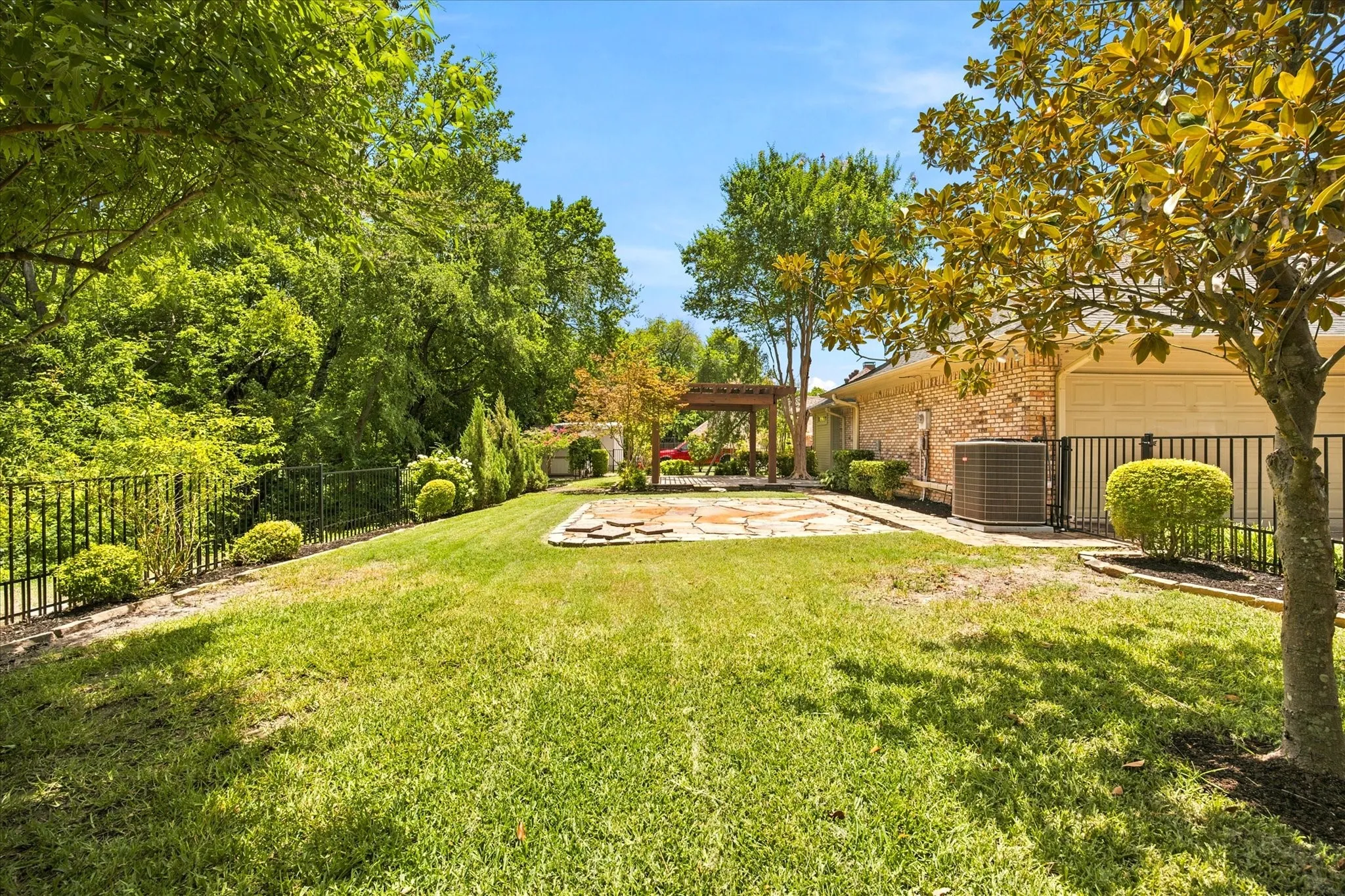 Expansive backyard featuring a stone paver patio, a freestanding wooden pergola, and mature trees