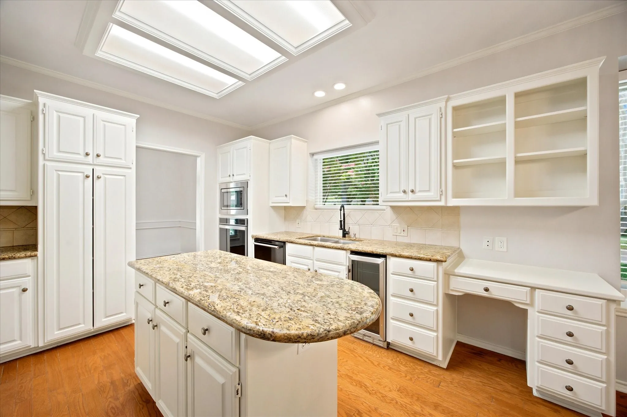 Kitchen featuring a central island with granite countertop, white cabinetry with silver hardware, wood-finish flooring, and a built-in desk area