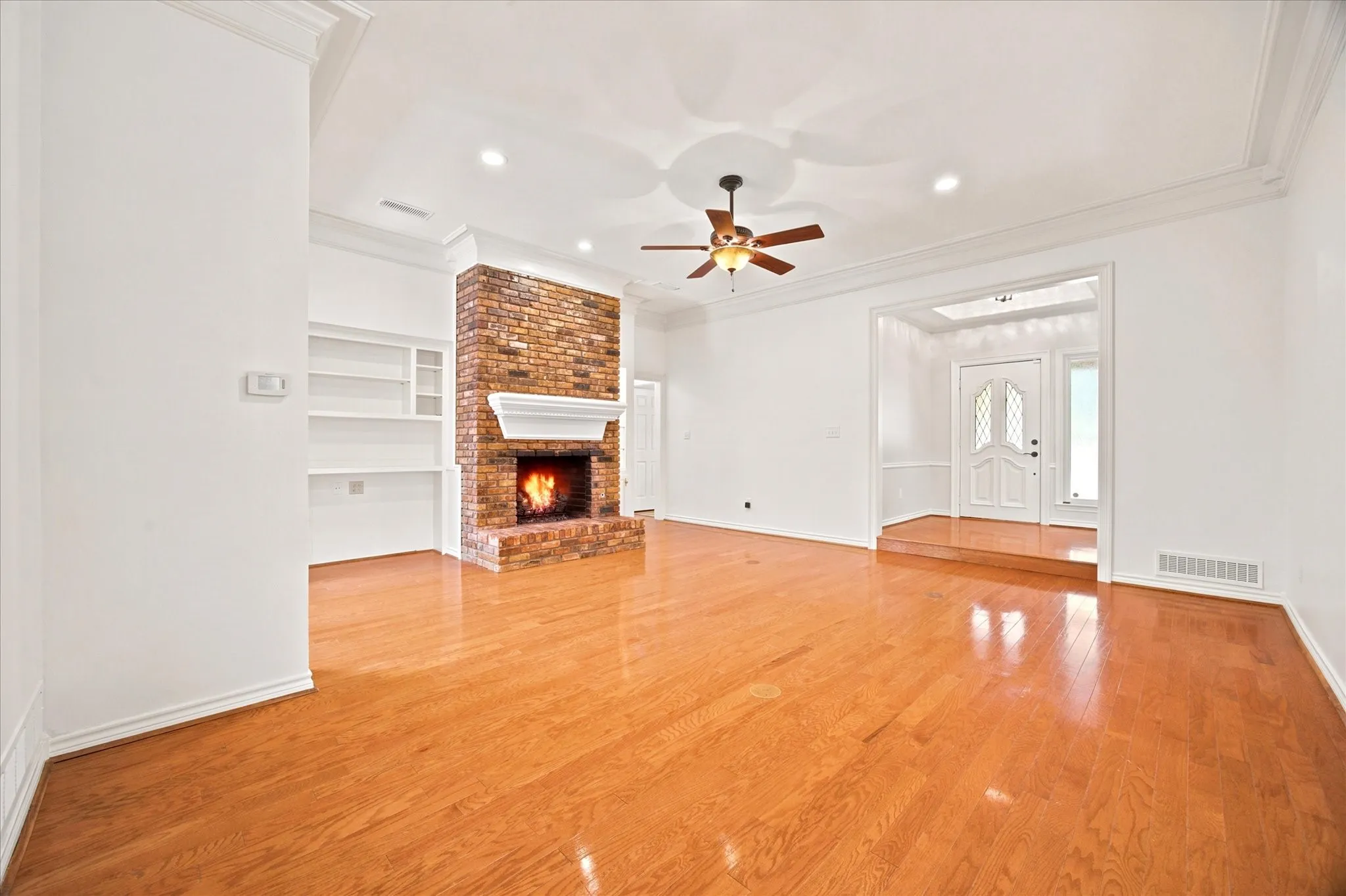 Spacious living area featuring polished wood-finish flooring, a brick-clad fireplace with a white mantel, and built-in shelving
