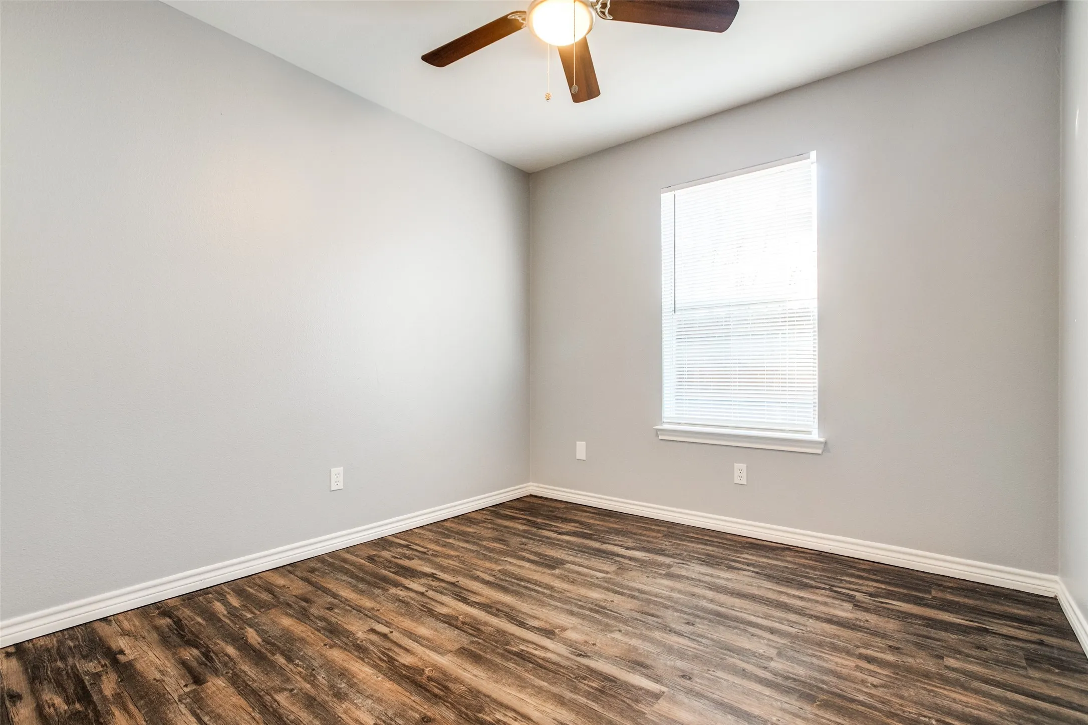 Room featuring wood-finish flooring, a ceiling fan with integrated lighting, and a window with blinds
