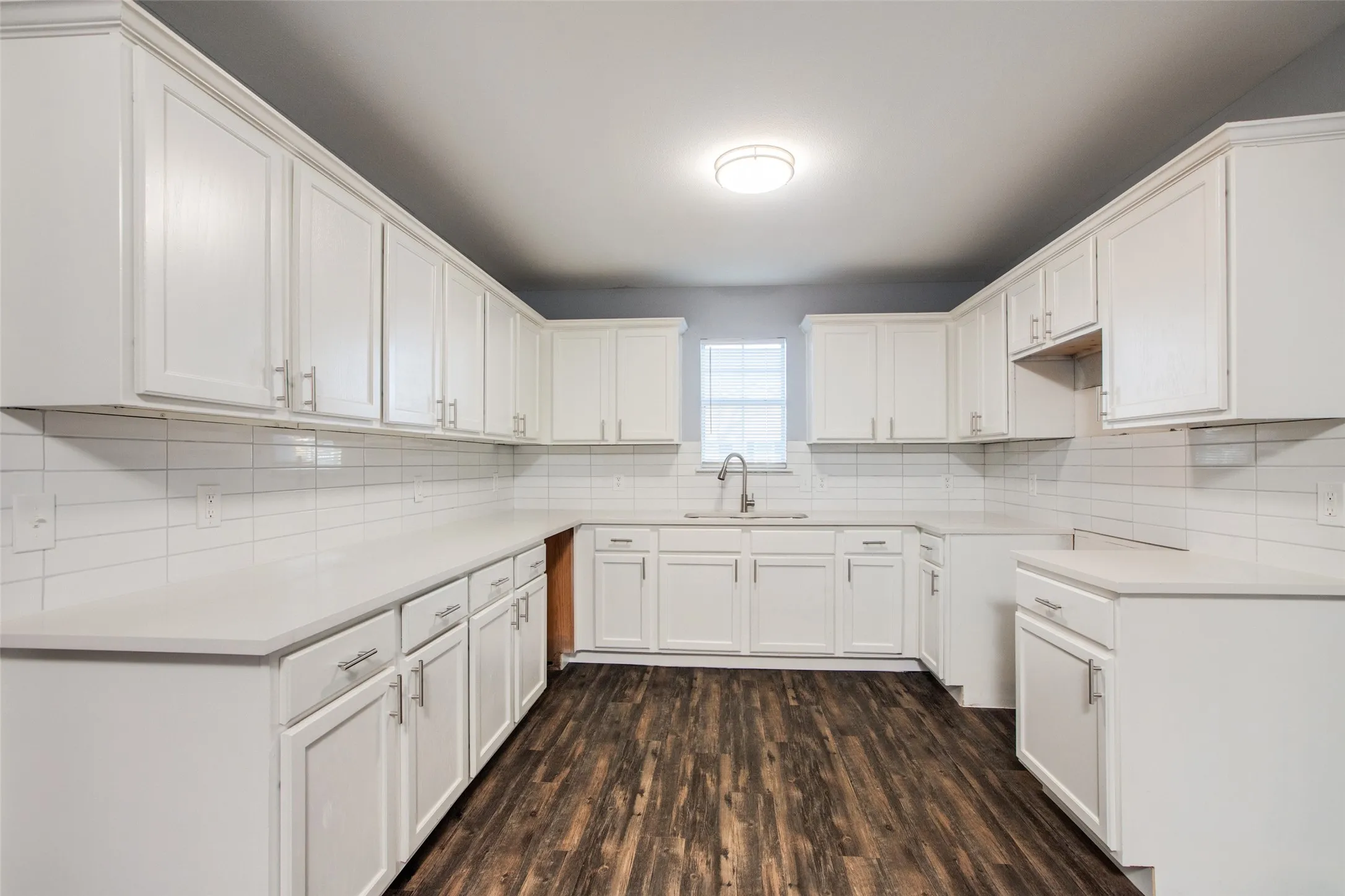 Kitchen featuring extensive white cabinetry, light countertops, subway tile backsplash, and wood-finish flooring