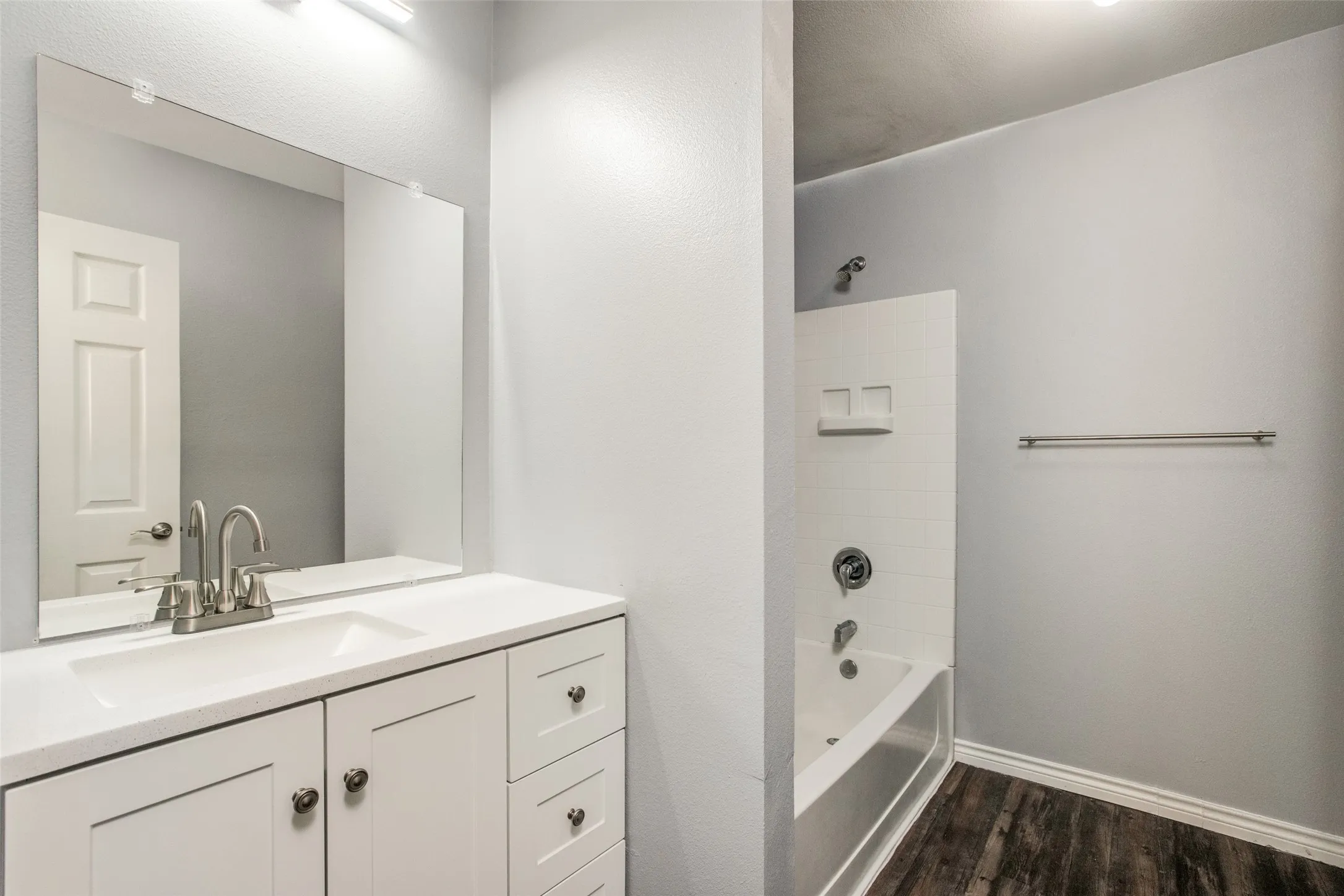 Bathroom featuring a white vanity with integrated sink, brushed nickel faucet, large mirror, and wood-finish flooring