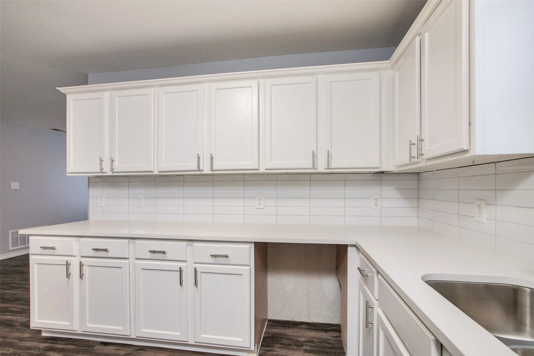White shaker-style cabinetry with crown molding, light-toned countertops, a stainless steel sink, and a horizontal subway tile backsplash