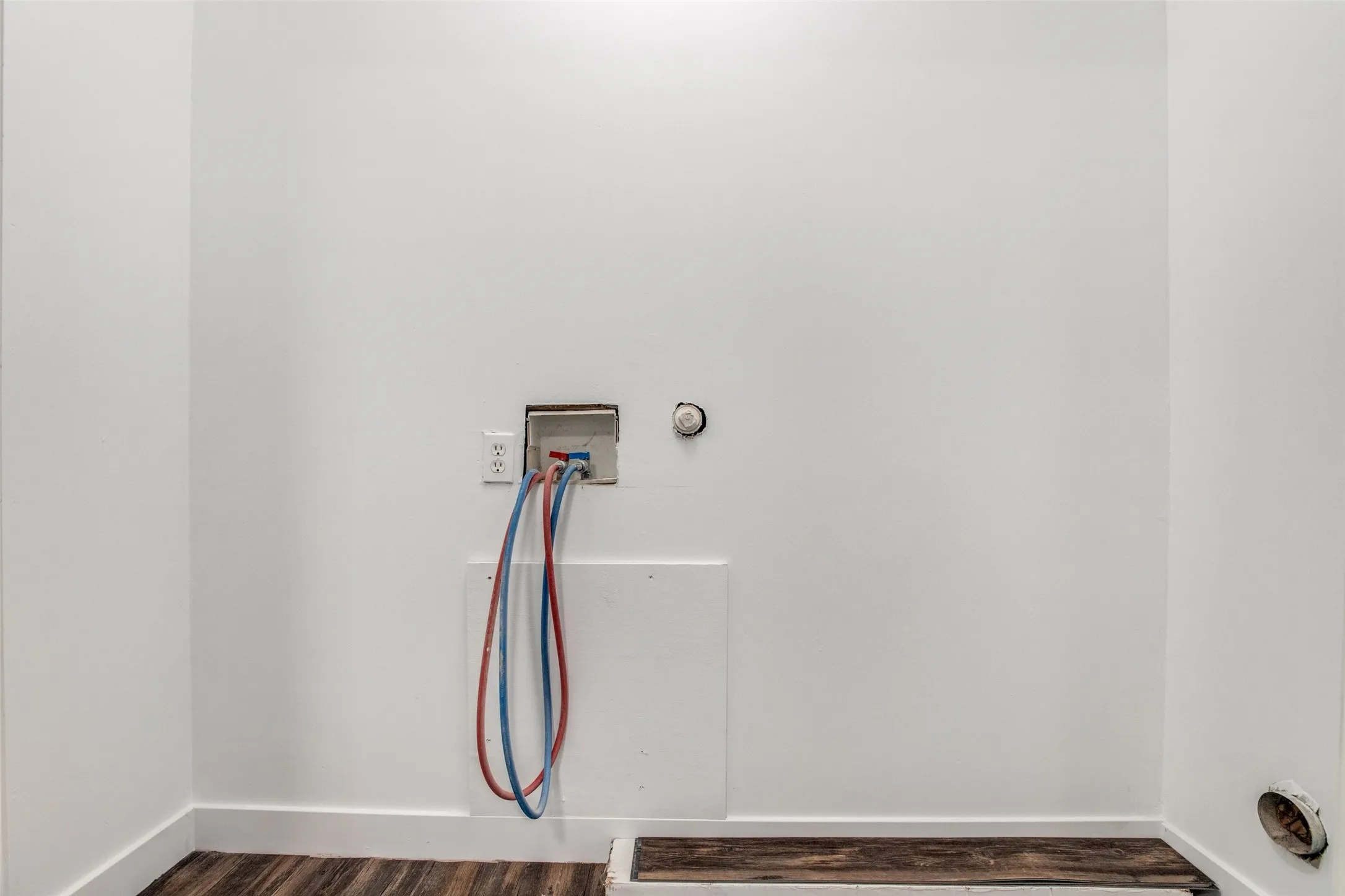 Laundry area with wood-finish flooring, white walls, and base molding