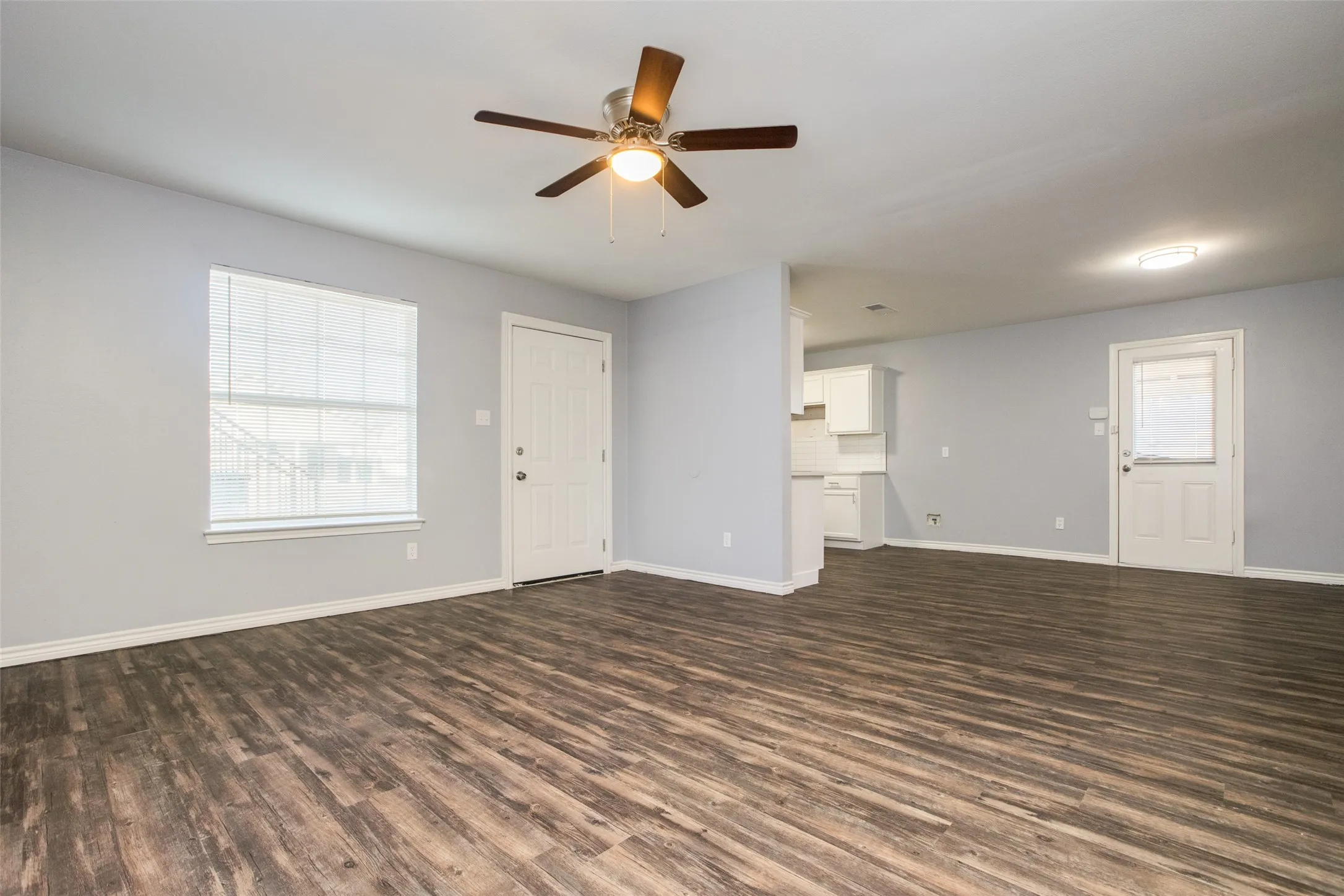 Expansive room featuring wood-finish flooring, light grey walls, and a ceiling fan with integrated lighting