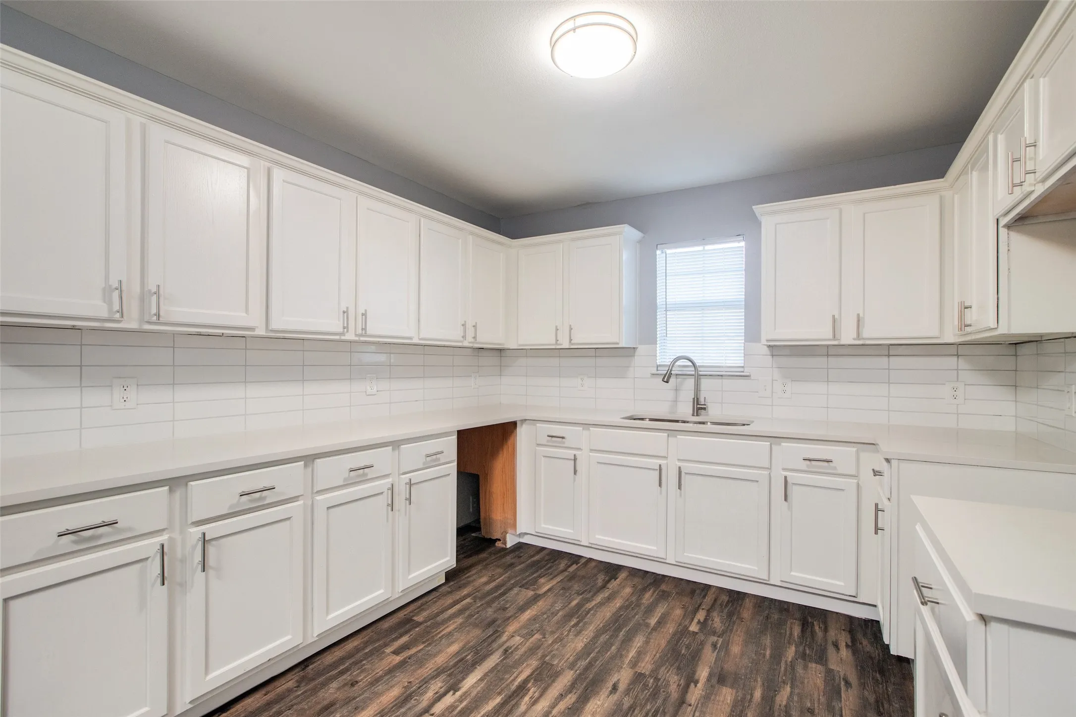 Kitchen featuring white shaker-style cabinetry with brushed nickel hardware, light-toned countertops, and a white subway tile backsplash